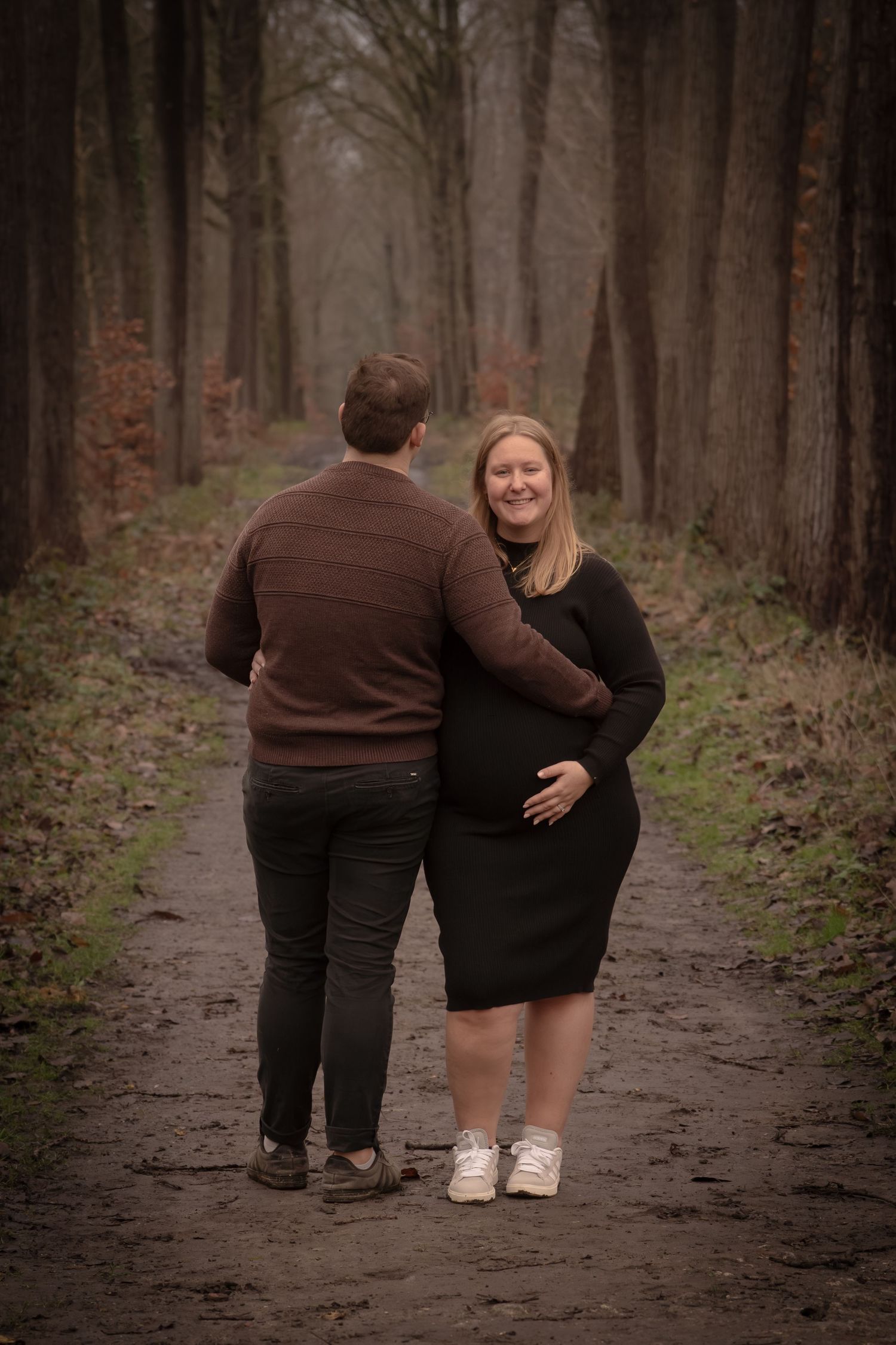 Two people walk together down a misty forest path in matching brown and black outfits.