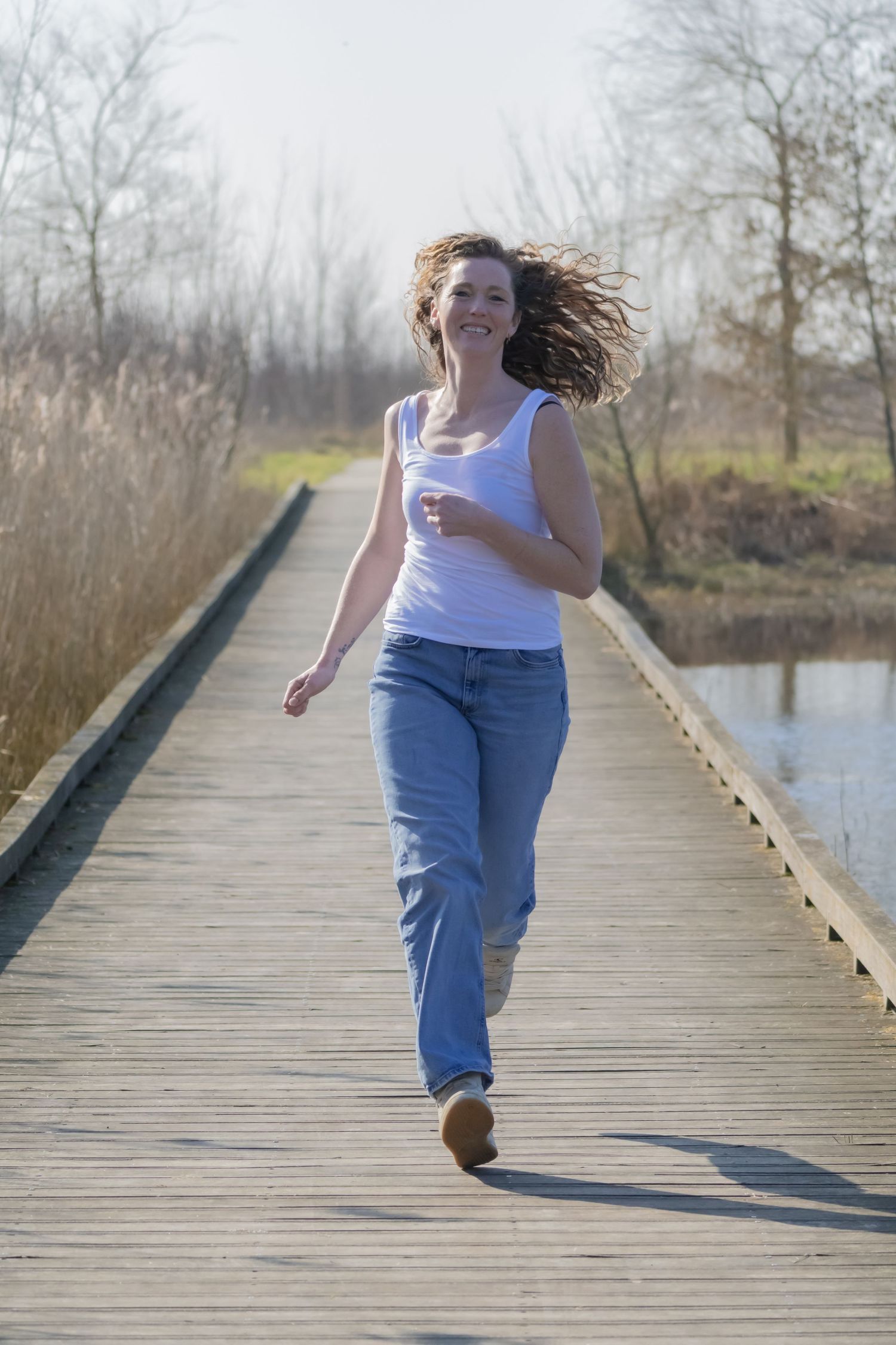 Person with flowing hair runs joyfully along a wooden boardwalk over water.