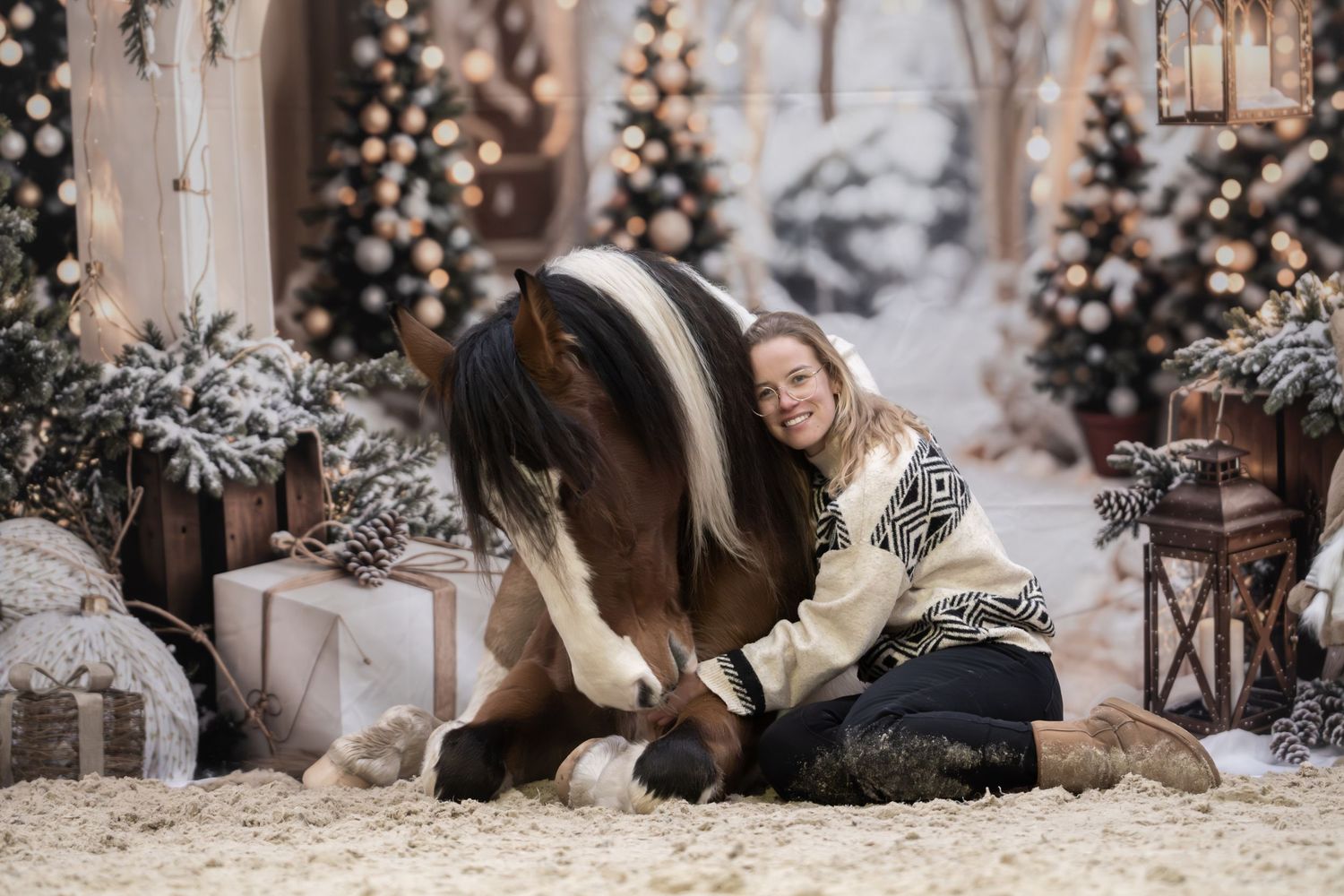 A cozy winter scene with a person in a knit sweater sitting next to a paint horse among Christmas decorations and gifts.