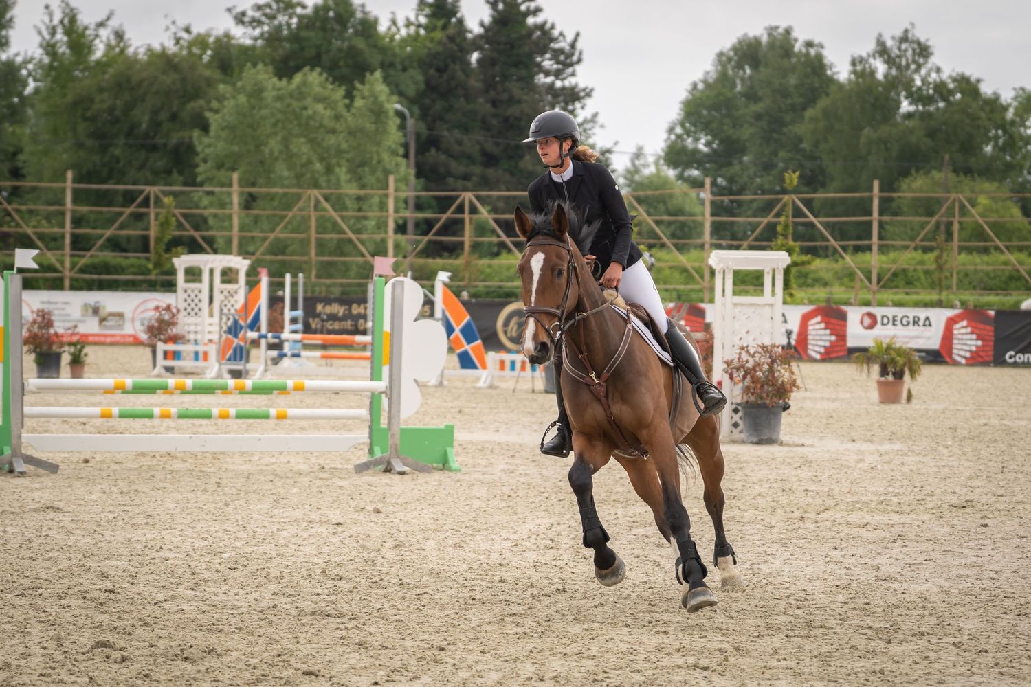 Equestrian athlete jumping over obstacle during competition in sandy arena.