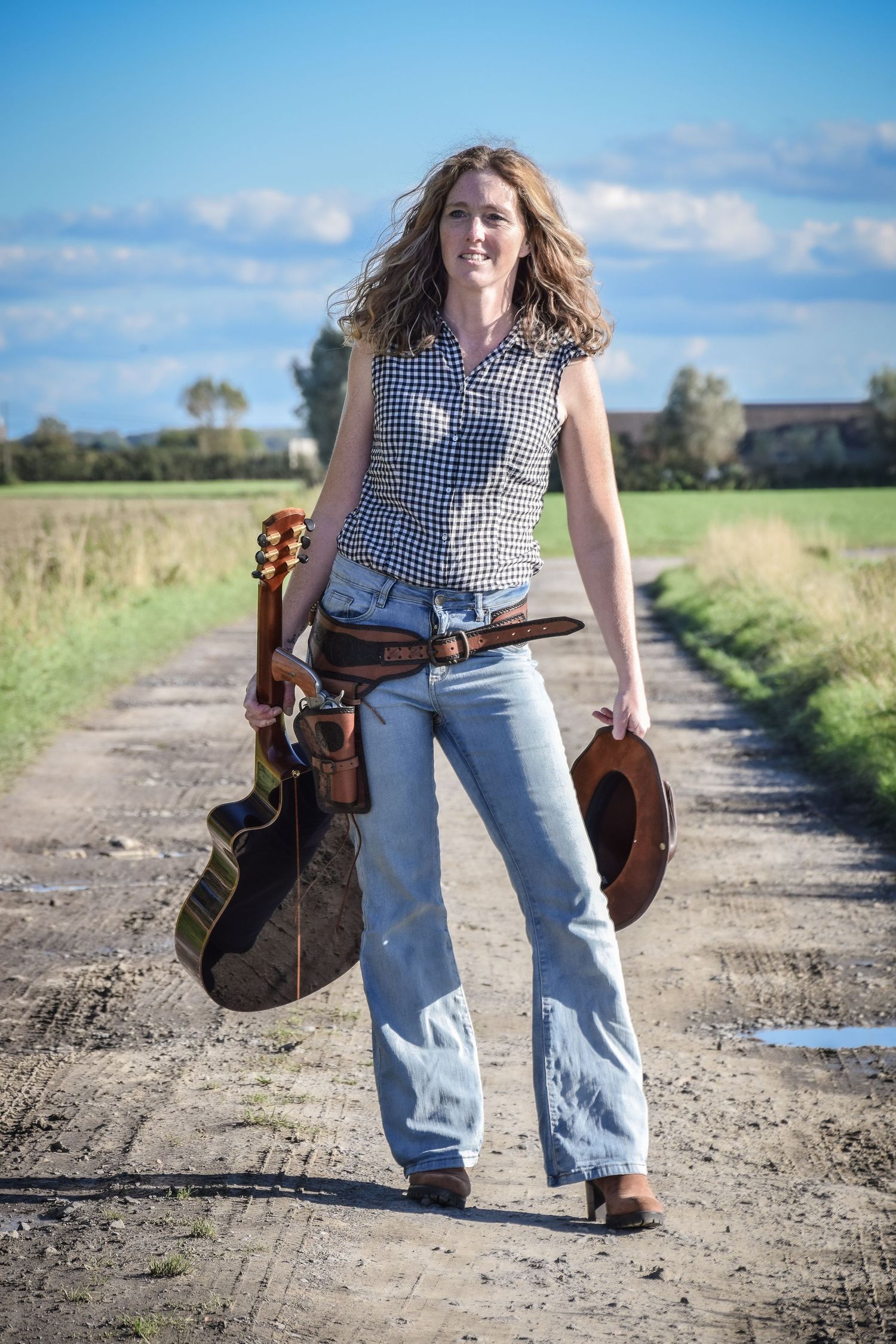 Walking sequence on a dirt path carrying a guitar and wearing country-style attire.