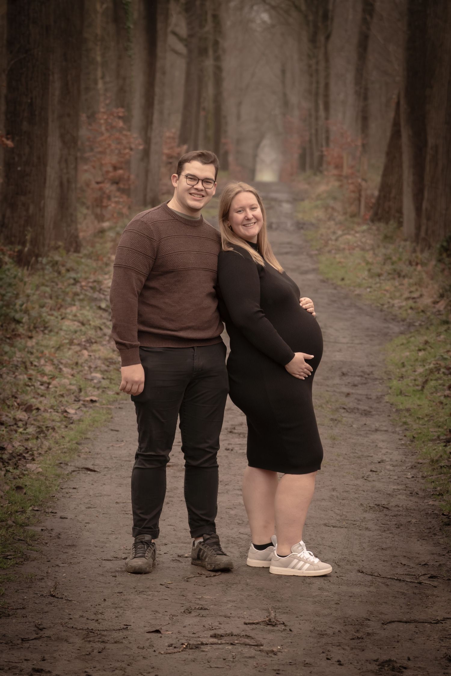 A couple in dark clothing stands together on a forest path in autumn, shown in a series of four similar poses.