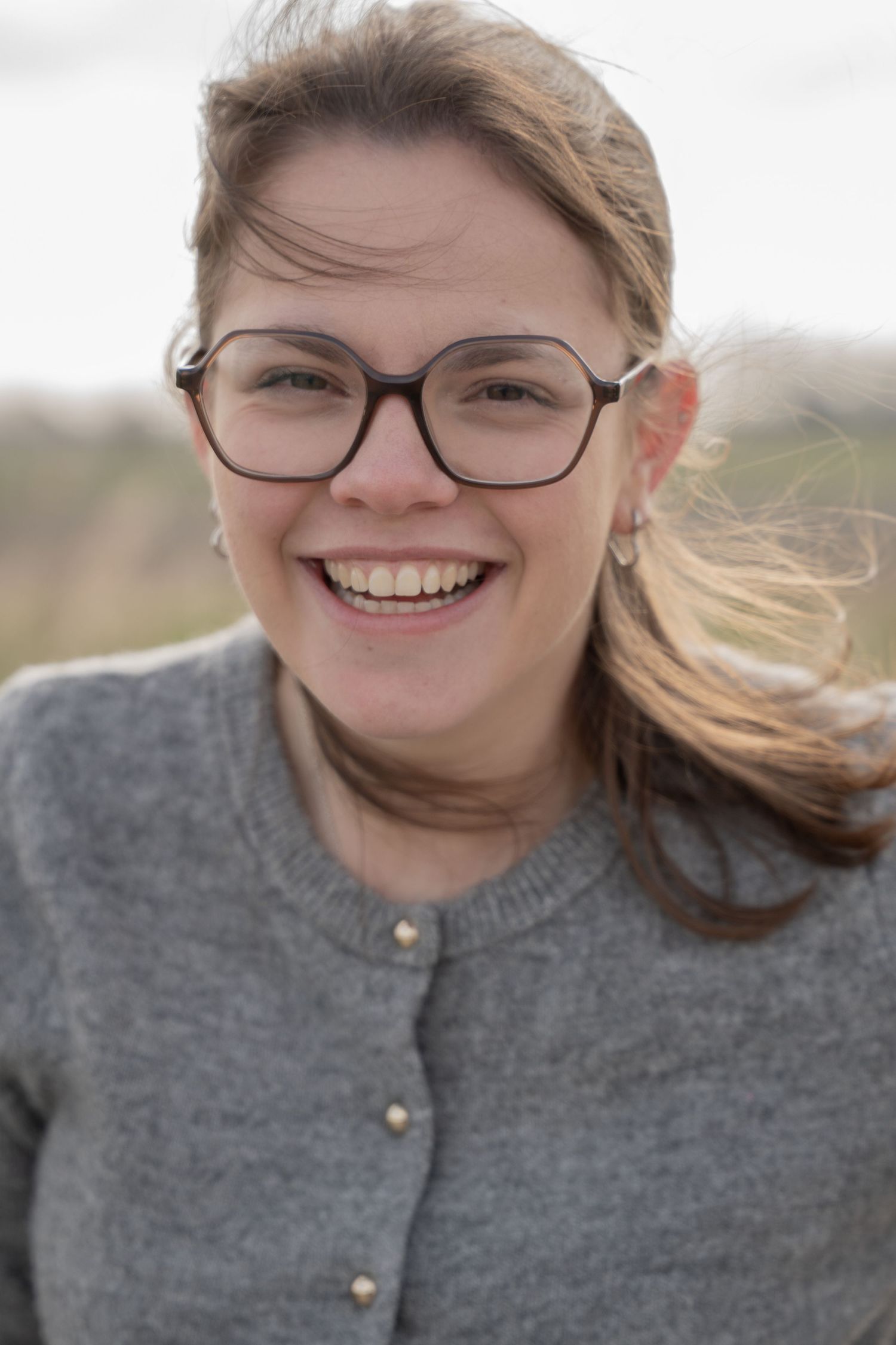 Close-up portrait with glasses and gray cardigan showing joyful expression outdoors.