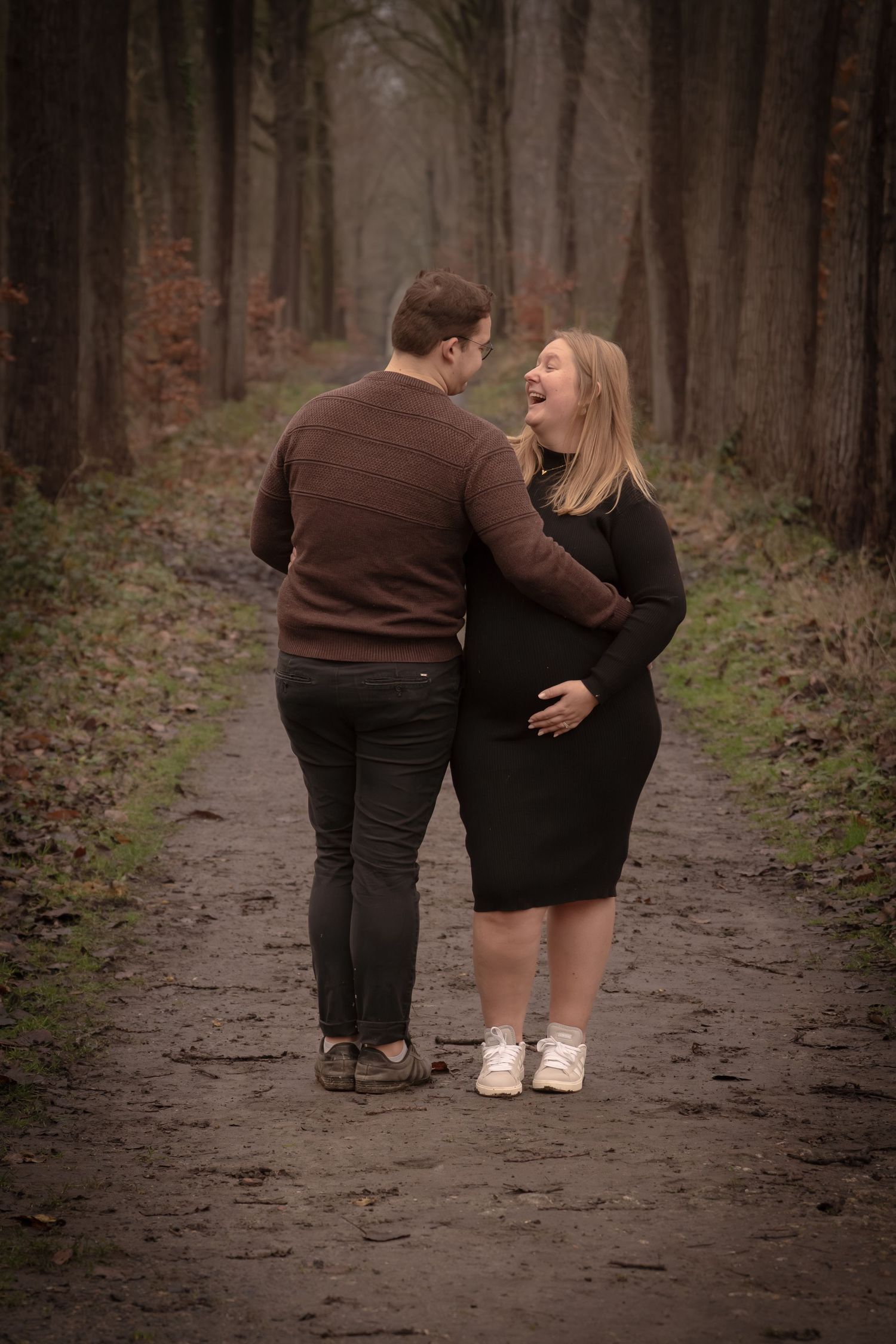 A couple in dark clothing shares an intimate moment while walking along a misty forest path in autumn.