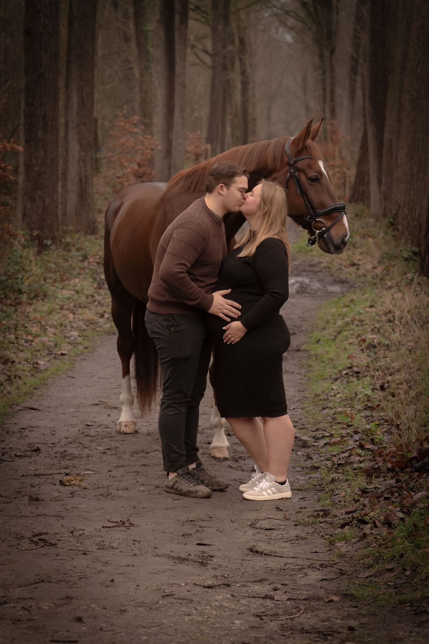 A couple shares a tender moment with their horse on a misty forest path during an engagement photoshoot.