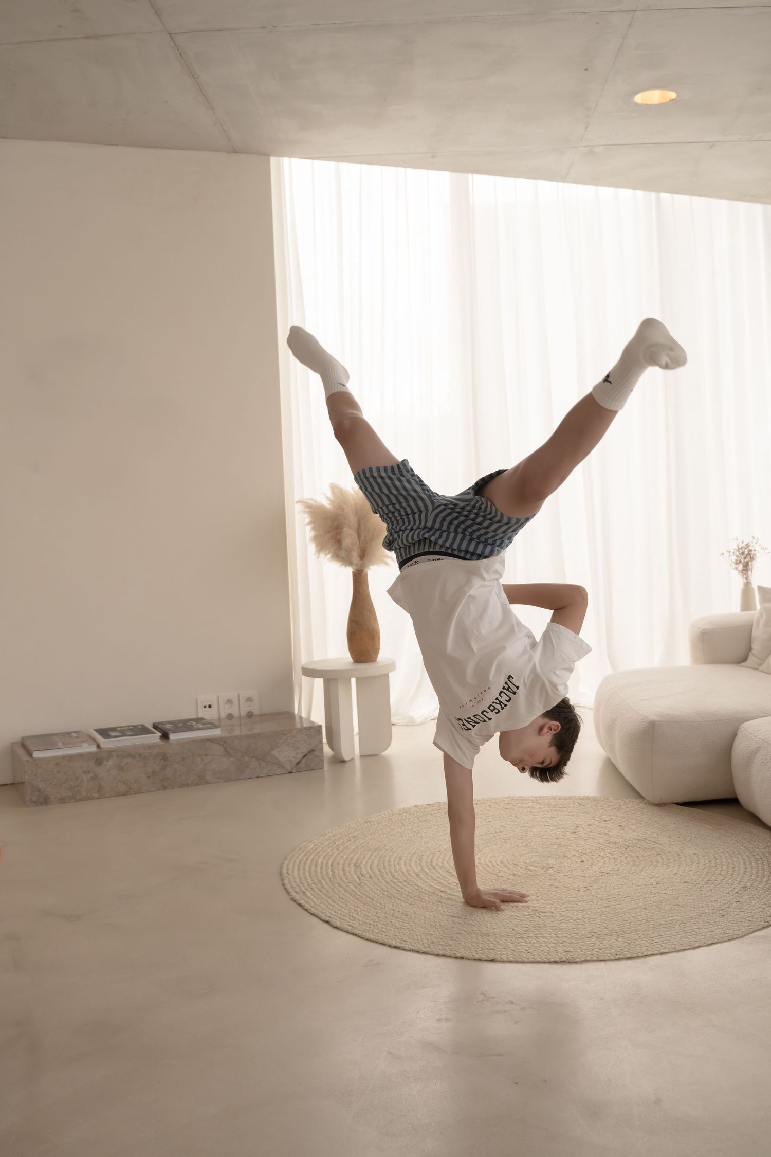 Person performing dynamic handstand movements on a circular rug in a minimalist white room.