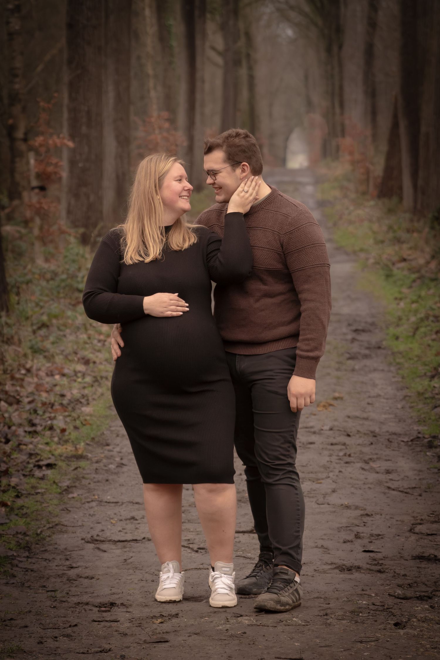 A couple shares an intimate moment while walking together on a wooded path in autumn.