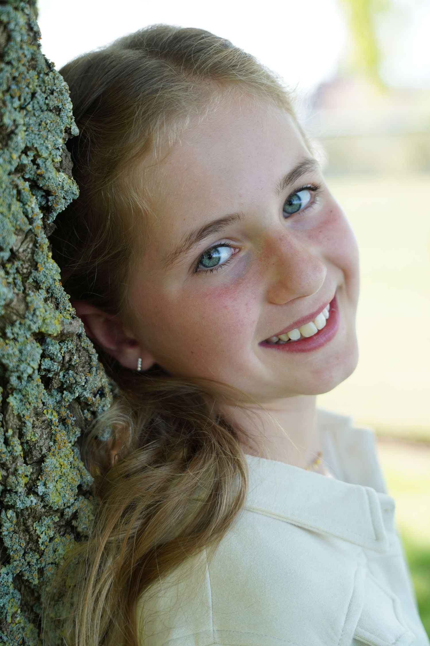 A young portrait photograph of someone leaning against a tree trunk outdoors.