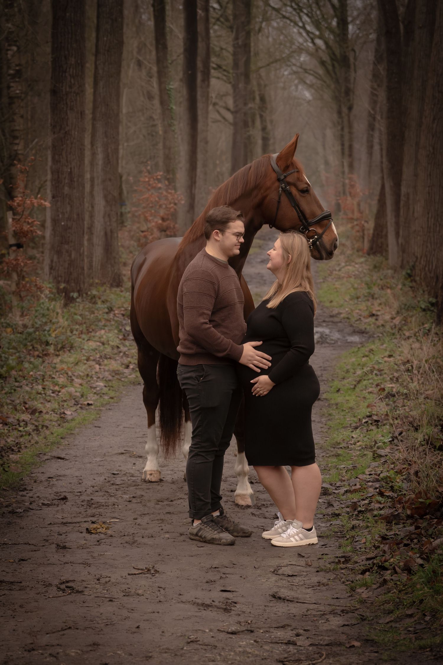 A couple embraces near their brown horse on a misty forest path during an autumn engagement photoshoot.