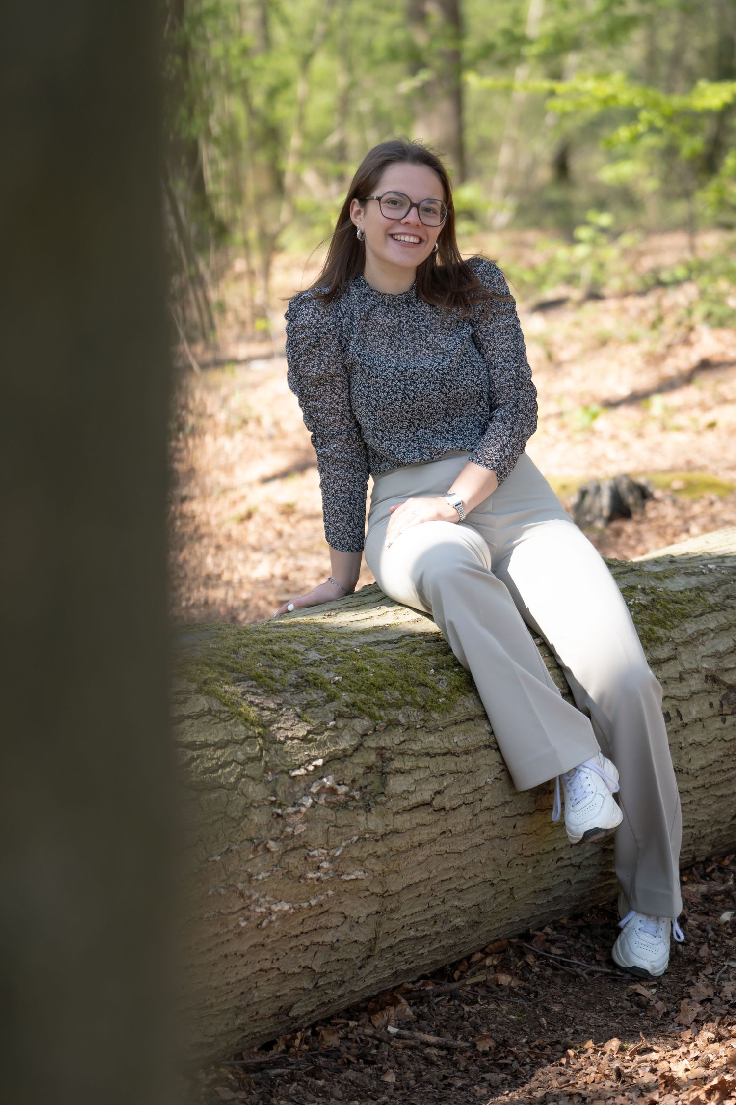 meisje poseert in het bos zittend op een boomstam