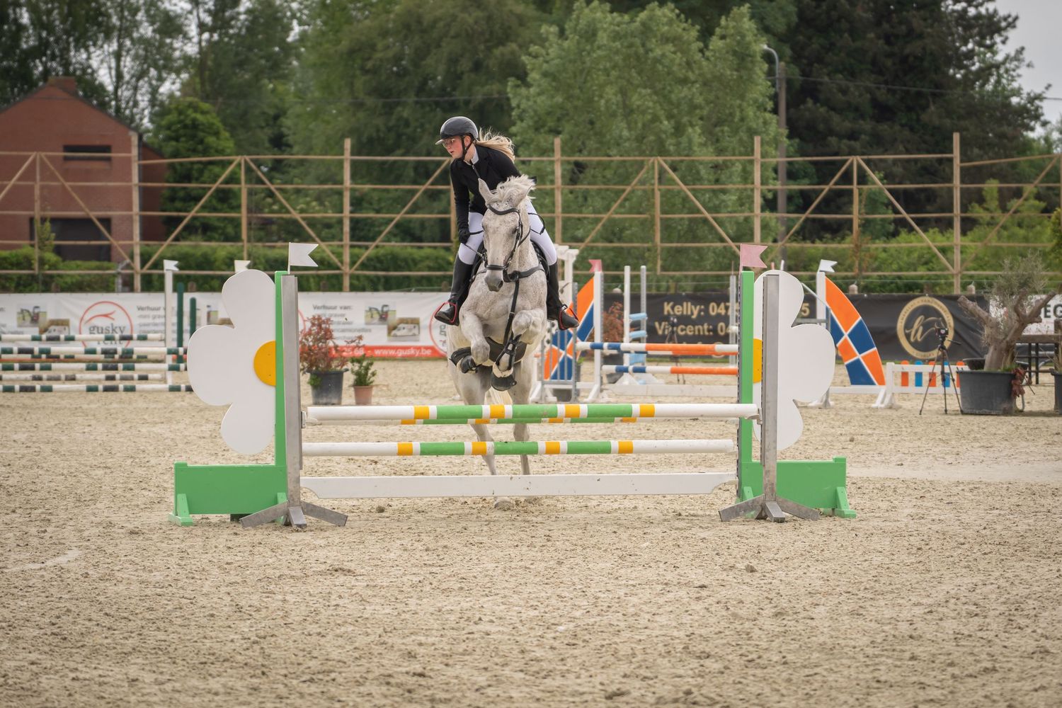 Horse and rider clearing obstacle during show jumping competition in sandy arena.