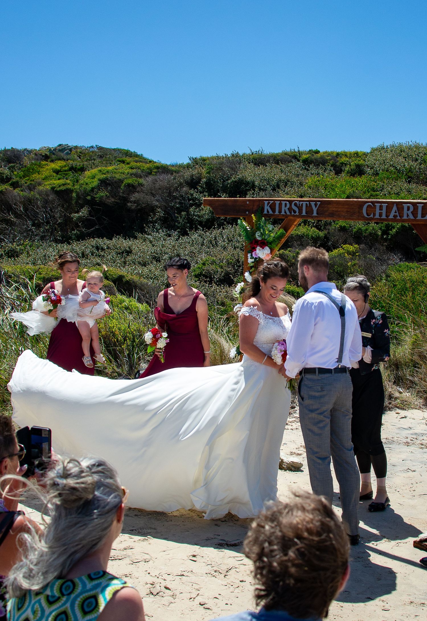 Beach wedding ceremony with flowing white dress and bridesmaids in burgundy dresses.