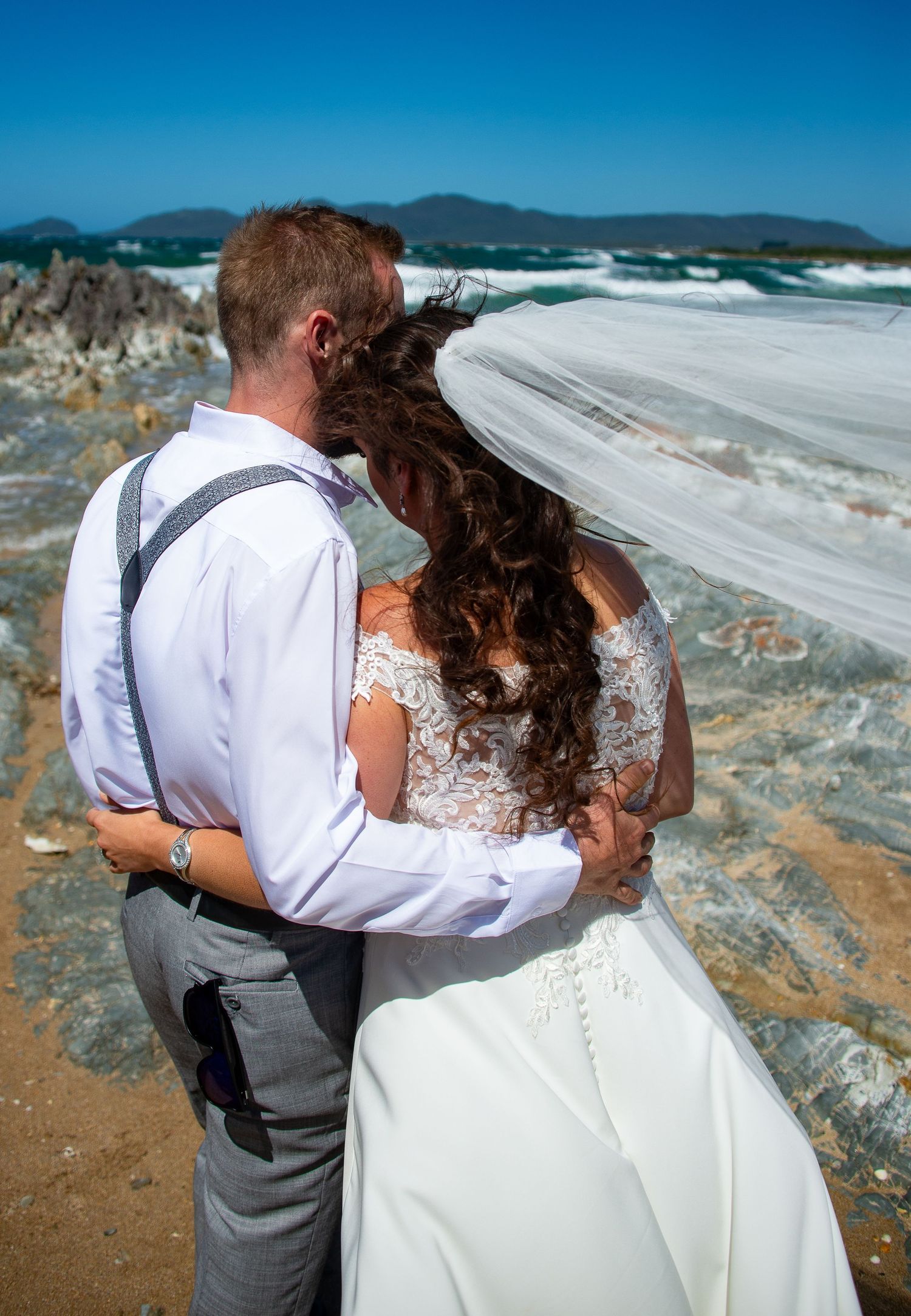 A scenic coastal wedding photo with mountains and ocean waves in the background.