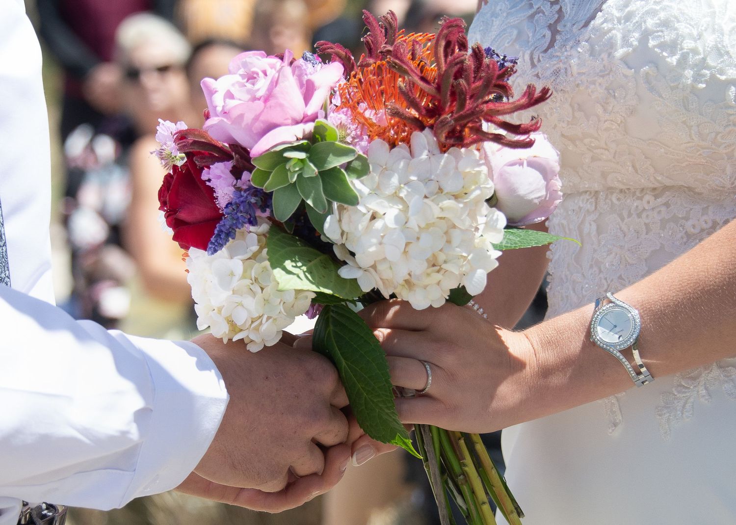 A colorful wedding bouquet with pink, red and white flowers being held by hands.