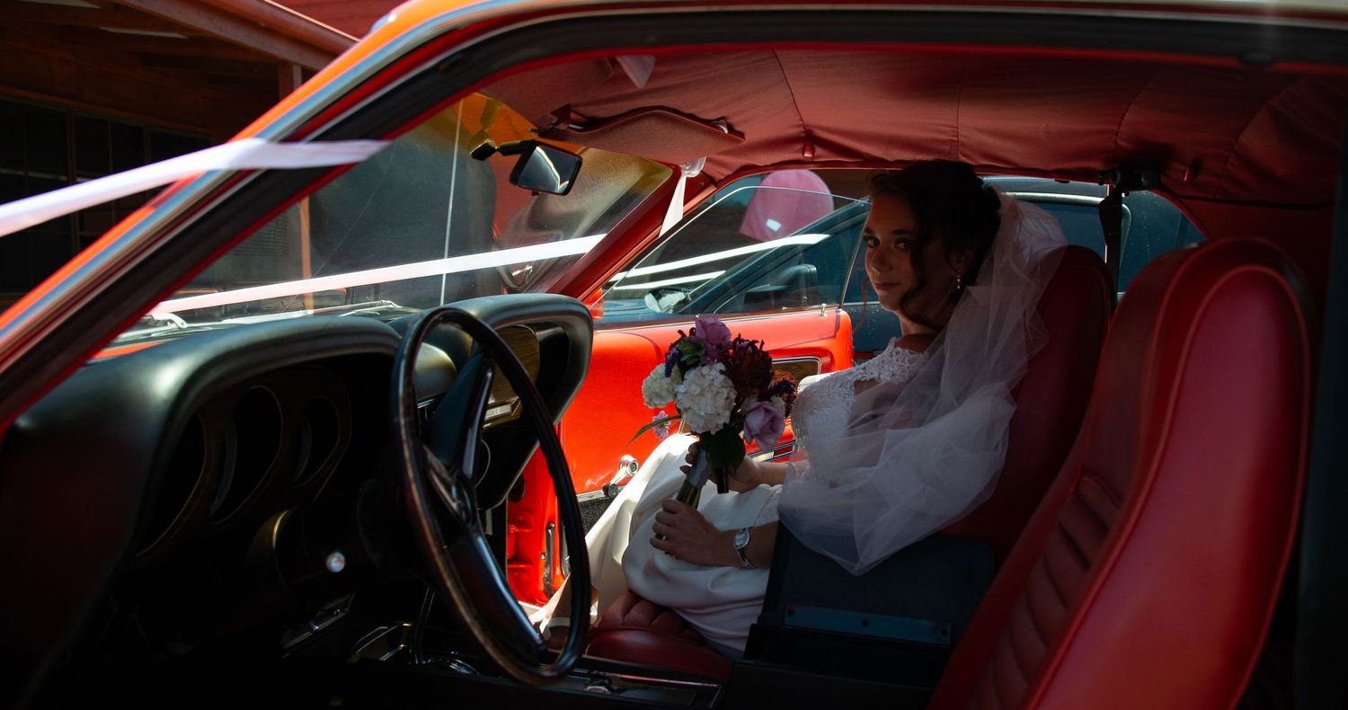 Bride sitting in vintage car with red interior.