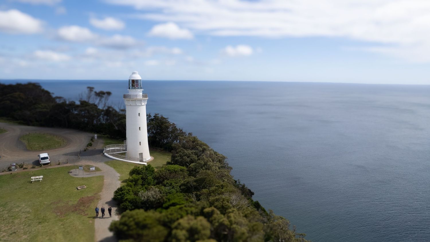 A white lighthouse stands tall on a coastal cliff overlooking the vast blue ocean.