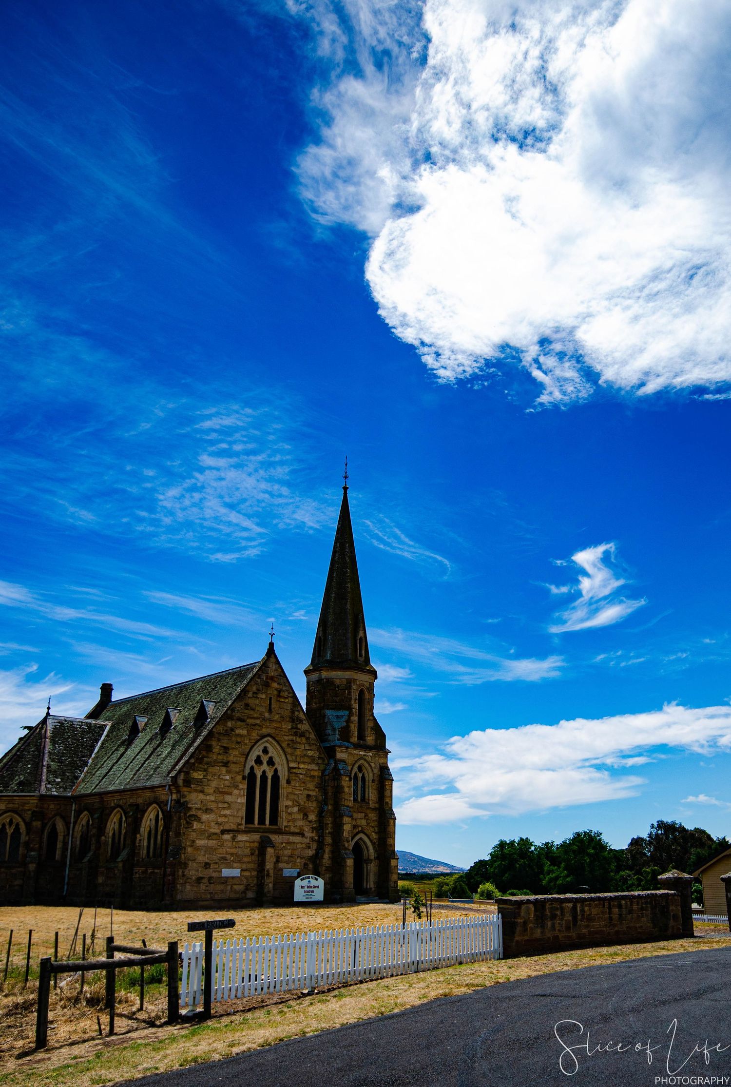 Gothic stone church with tall spire against bright blue sky with white clouds.