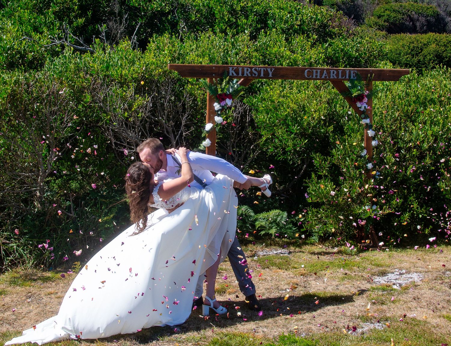 A romantic wedding moment captured under a floral arch in a garden setting.