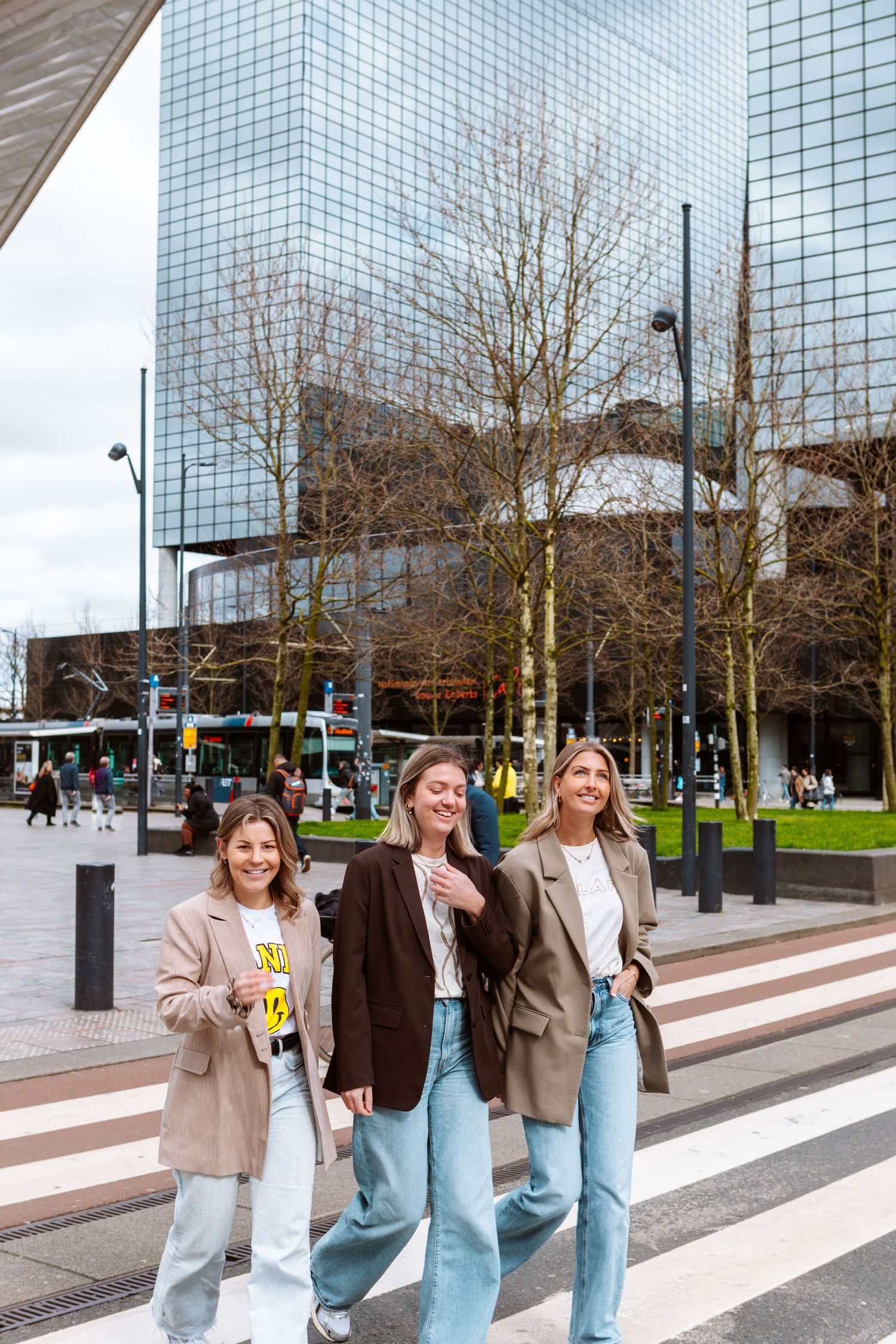 Group walking across street with modern glass building and trees in background.