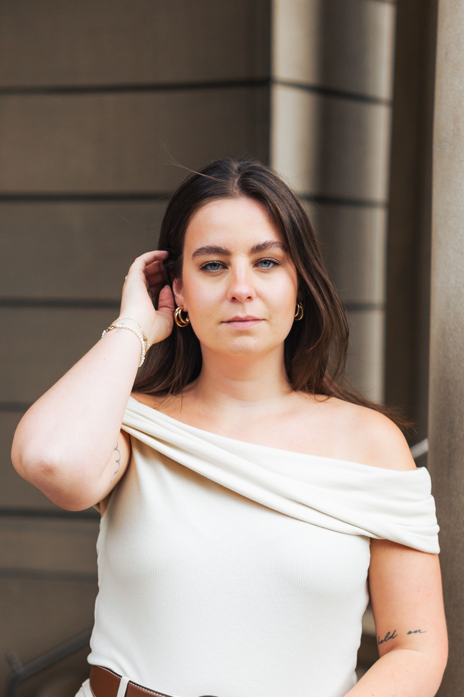 Woman in white off-shoulder top poses elegantly against neutral background.