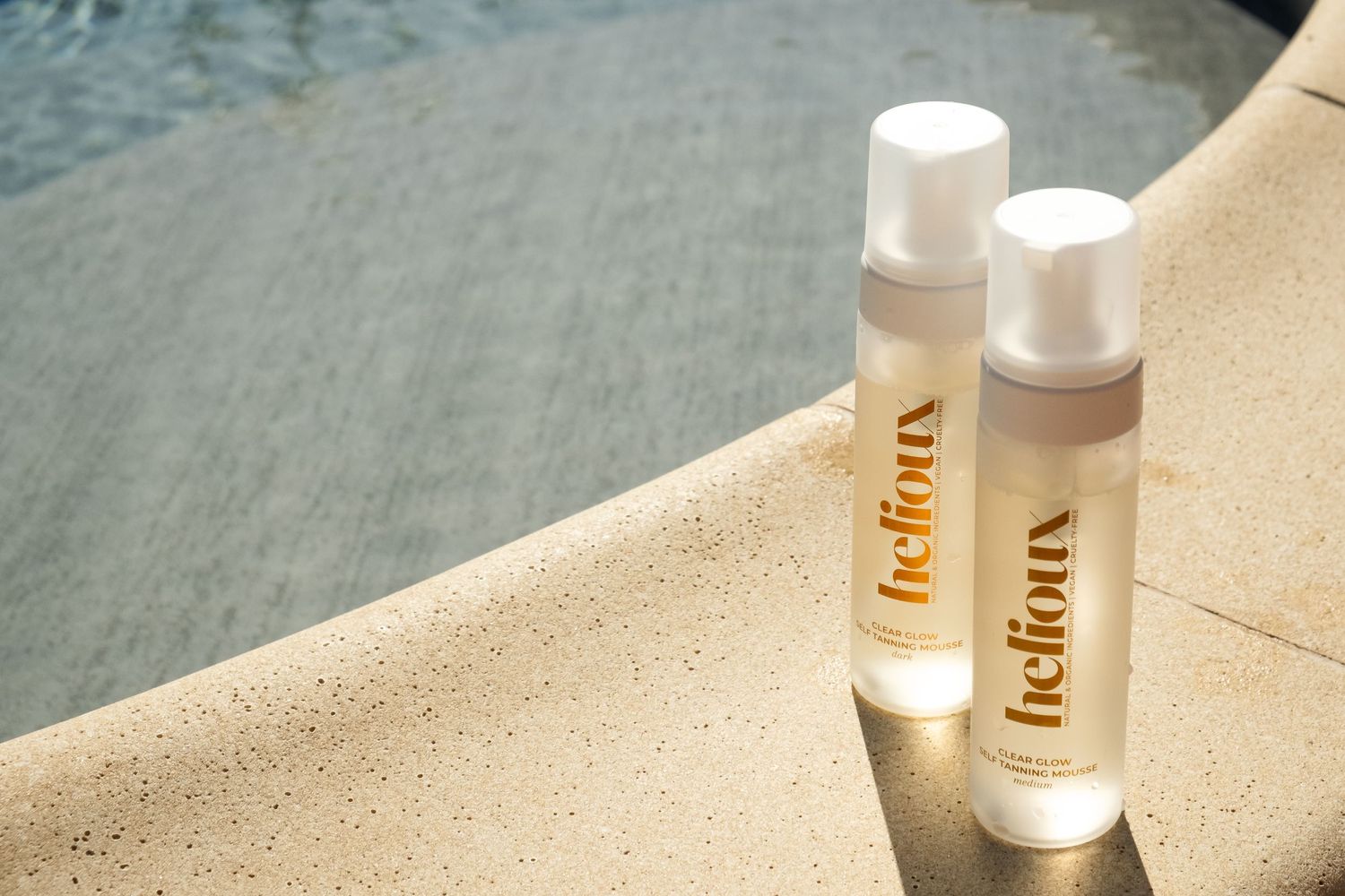 Two white skincare product bottles positioned on beige surface in sunlight.