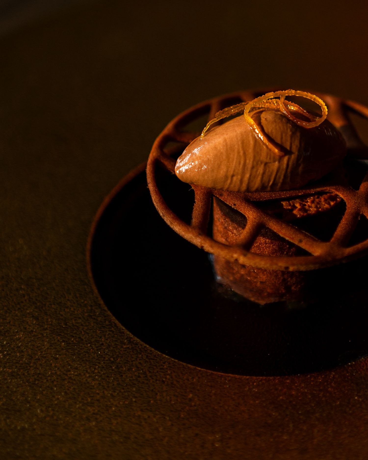 Dark and moody photograph of a pastry with decorative chocolate swirls on a black plate.