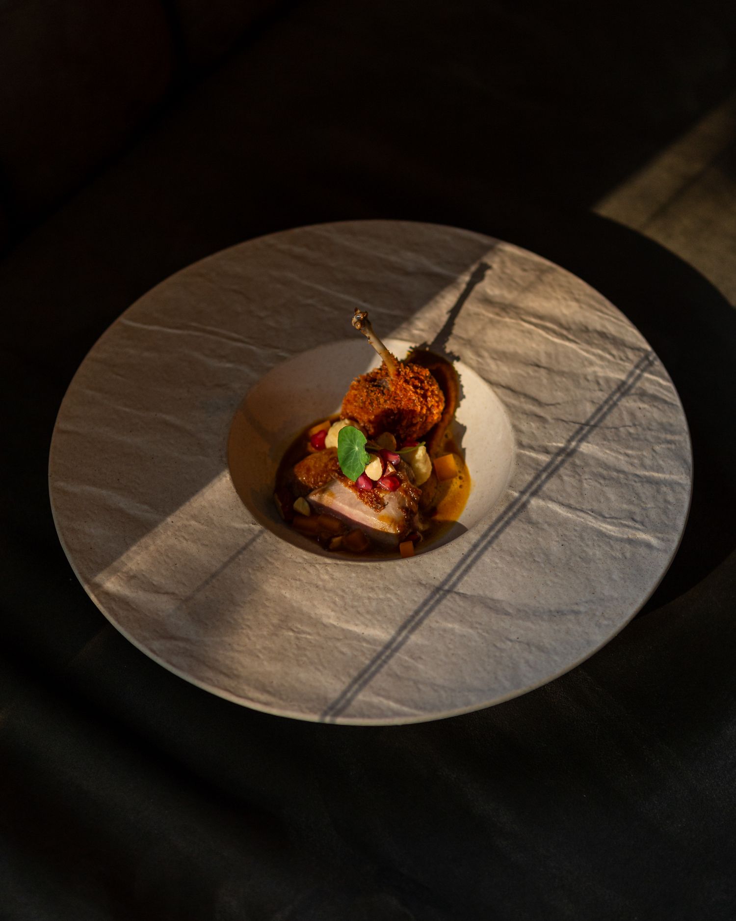Elegant plated dessert with garnish on a textured white plate in dramatic lighting.