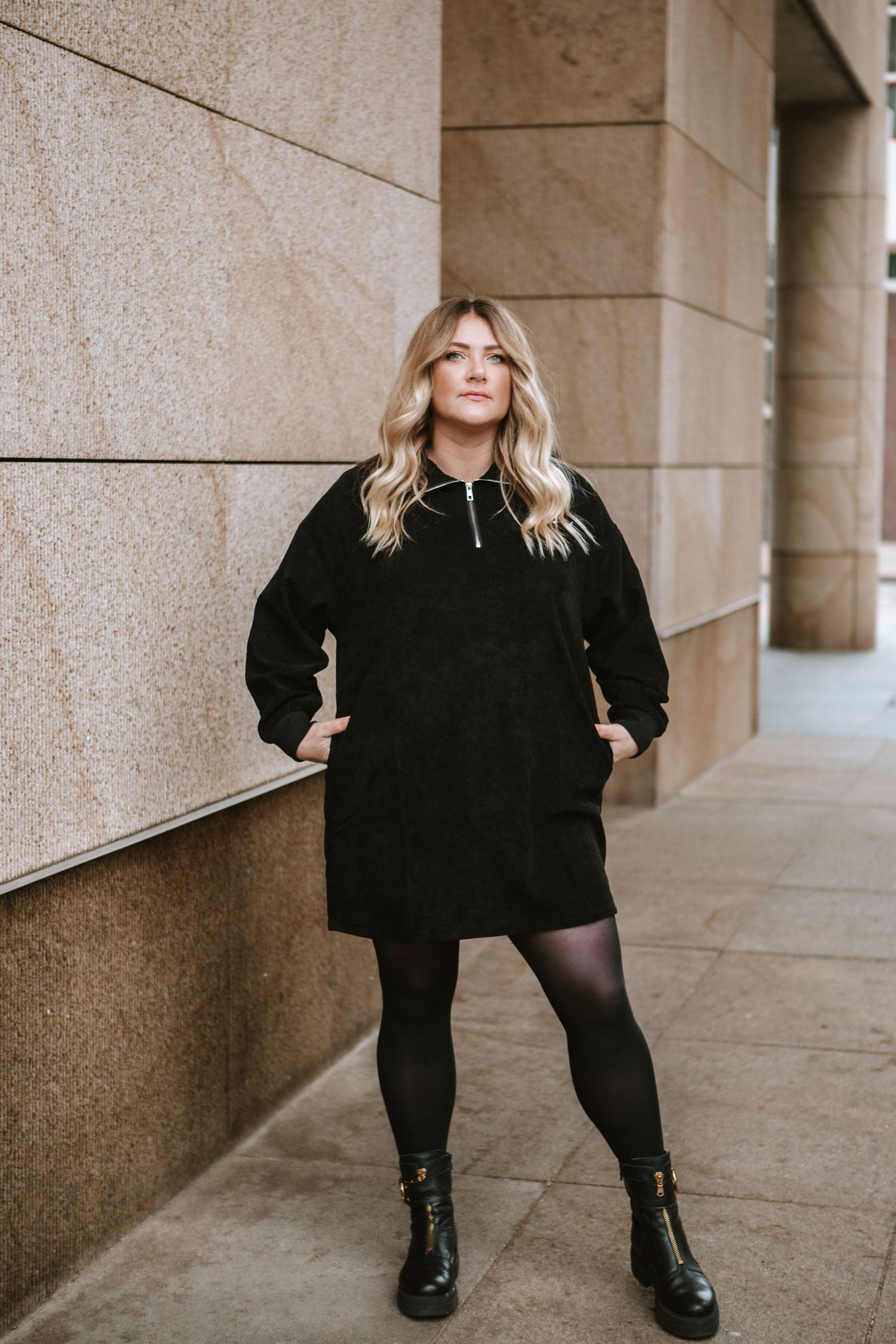 Winter street style with black coat, tights and boots against stone architecture.