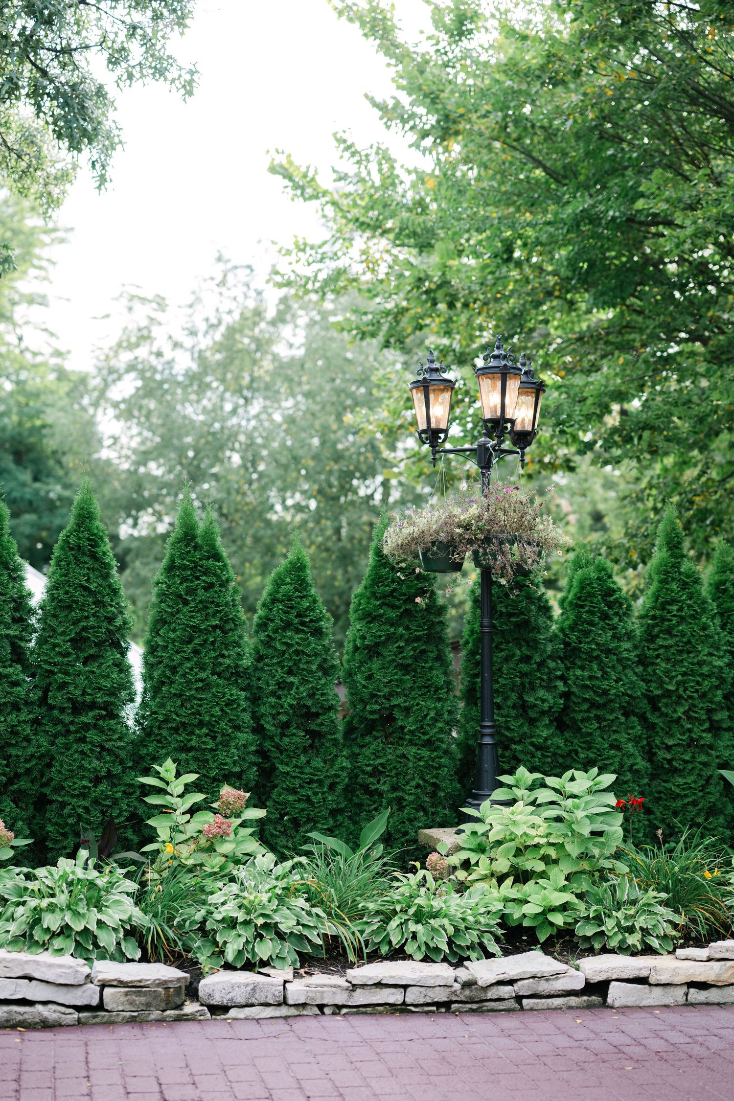 Decorative black lamp post illuminates a garden path bordered by evergreen trees and stone wall landscaping. - Meyer's Castle Events