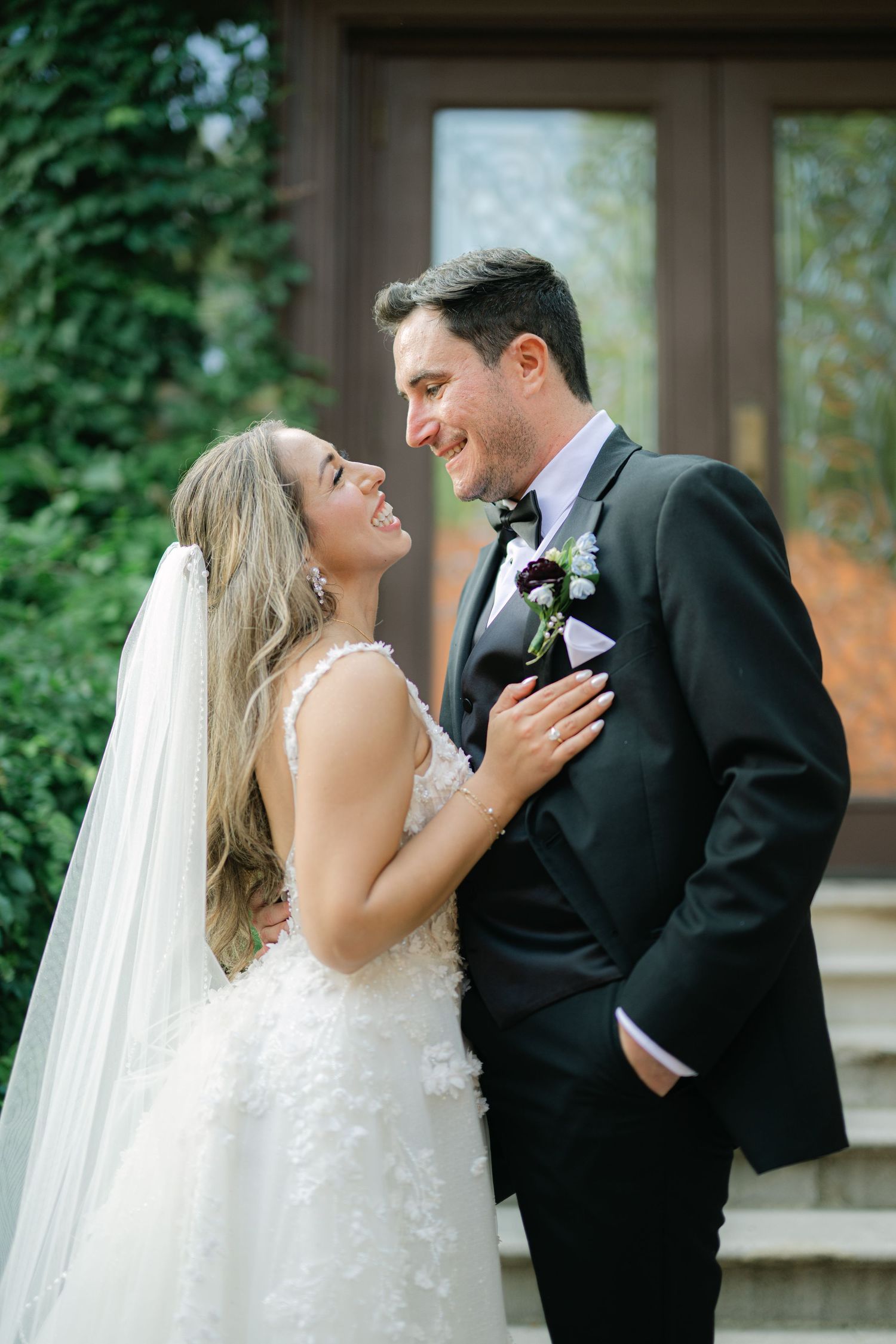 A bride and groom share a joyful moment together outdoors, with greenery and stone architecture in the background. - Meyer's Castle Events