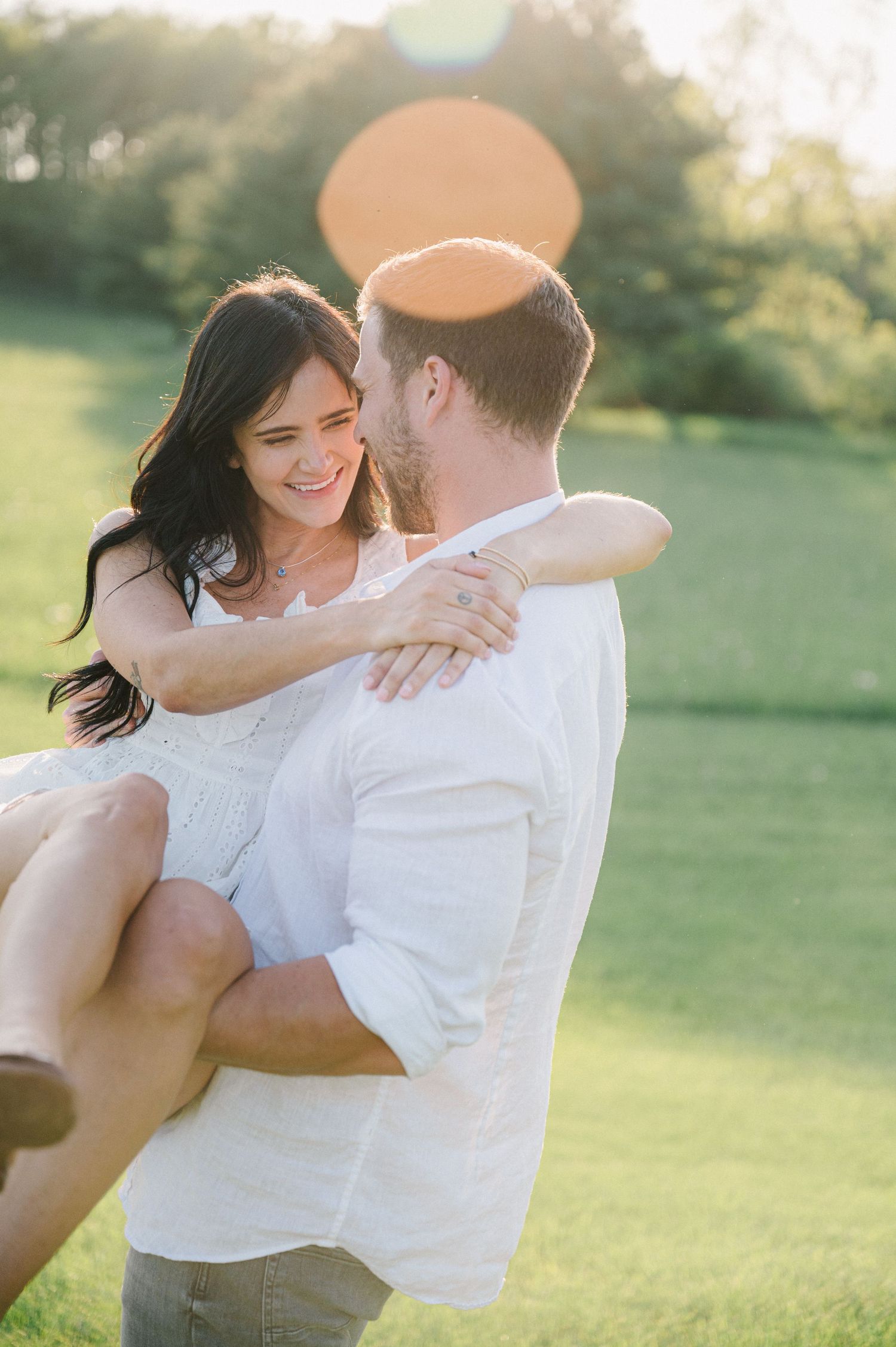 A couple embraces tenderly in a sun-drenched meadow during a romantic outdoor engagement session. - Oswego, IL