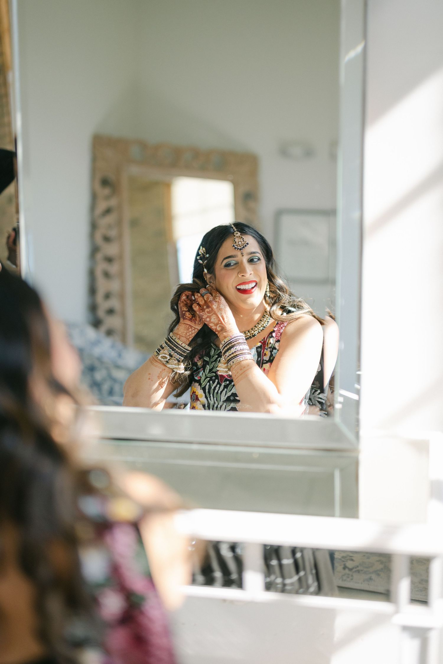 Reflection in mirror shows someone wearing traditional Indian jewelry and makeup while getting ready. - The Brix on the Fox
