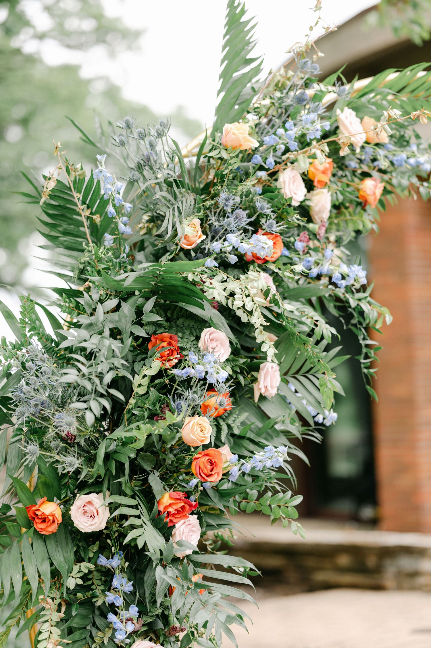Lush floral arrangement with coral and blush roses mixed with ferns and delicate blue flowers. - Hyatt Lodge Oak Brook