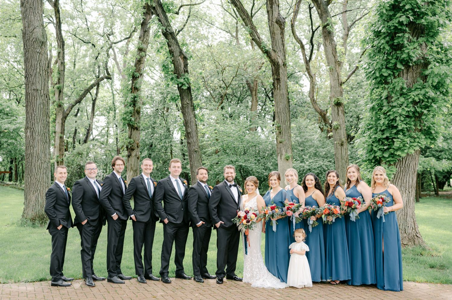 Wedding party in formal attire poses together in a scenic wooded outdoor setting with green trees and foliage. - Hyatt Lodge Oak Brook