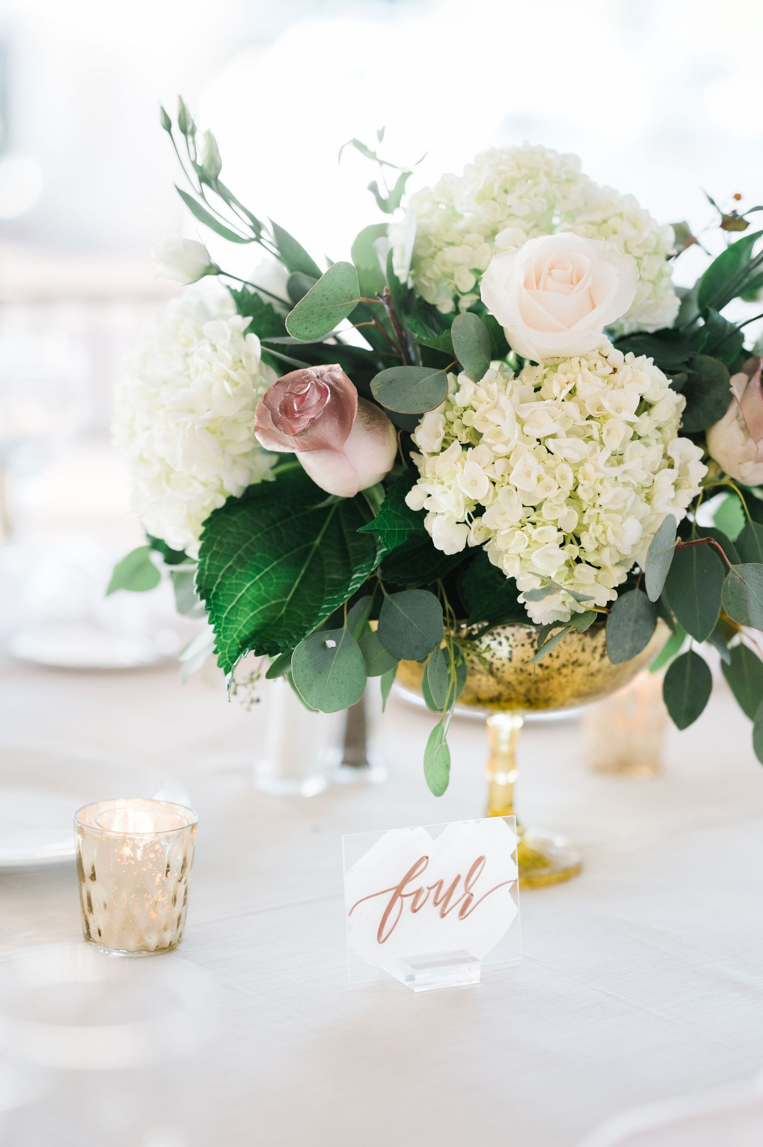 Beautiful white hydrangea and pink rose centerpiece in gold vase with table number.