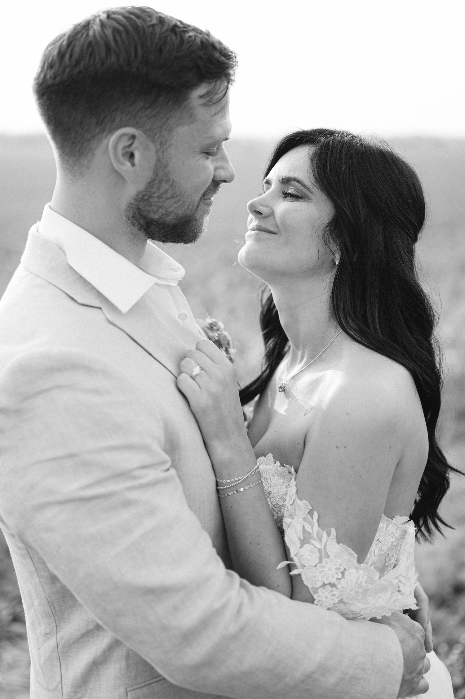A romantic black and white wedding portrait shows a couple embracing outdoors, with the bride in lace and groom in light attire.