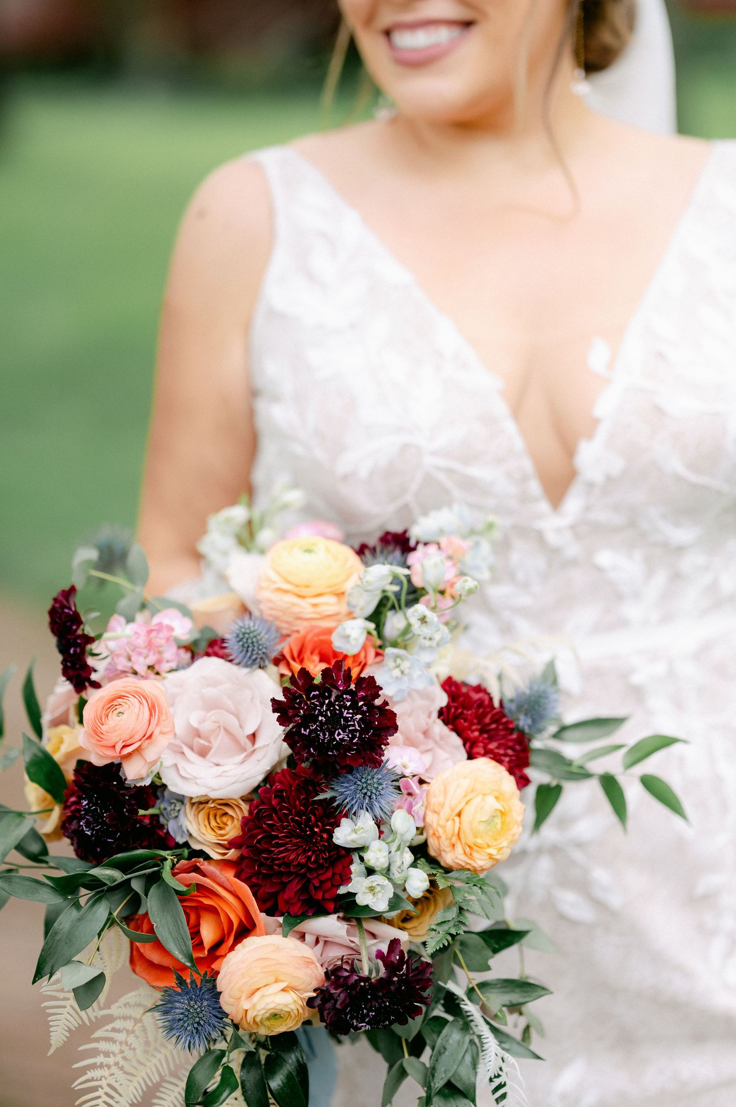 A stunning fall wedding bouquet features burgundy dahlias, peach and yellow roses, and eucalyptus against a white lace dress.