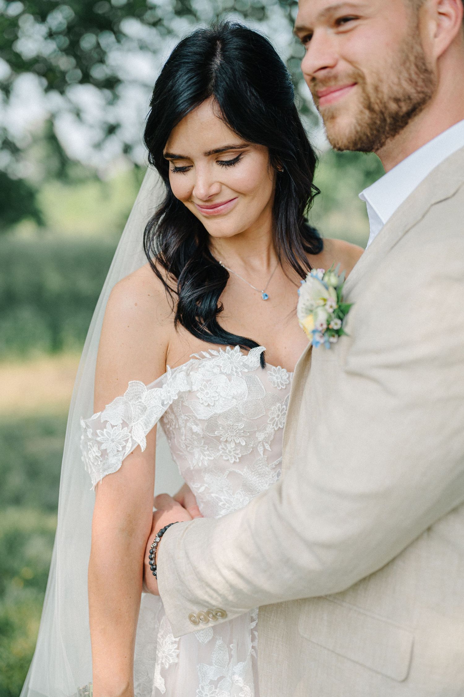 A close-up wedding portrait shows a couple embracing outdoors, with the bride wearing a delicate lace off-shoulder gown.