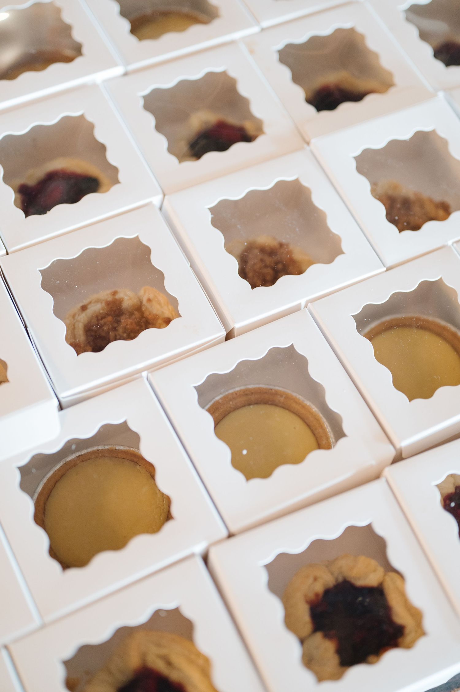 White bakery packaging boxes with cutout windows show various dessert fillings inside each compartment.