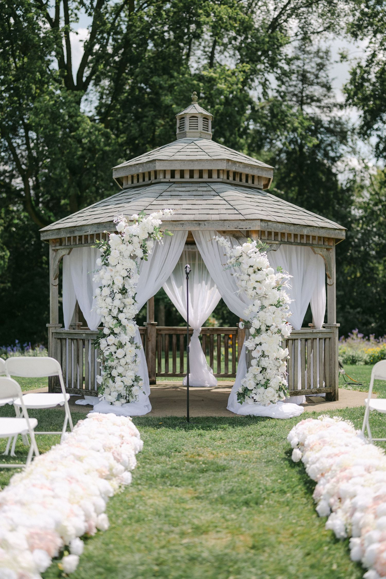 A white wooden gazebo decorated with floral arch and draped fabric for a wedding ceremony. - Bird Haven Greenhouse
