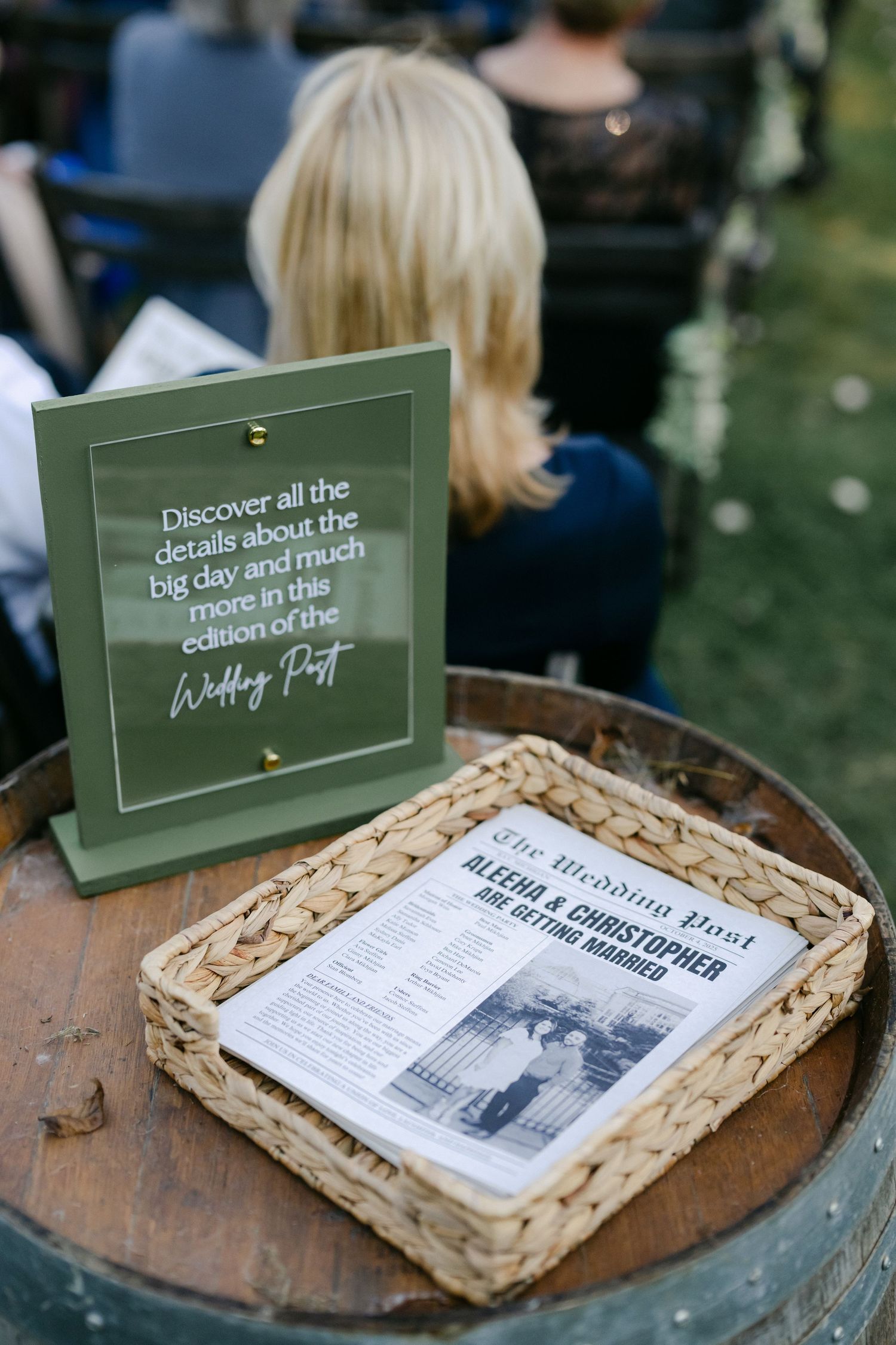 Wedding newspaper program and green sign on barrel at outdoor ceremony for Aleecha and Christopher's wedding. - Youngblood Vineyard Wedding