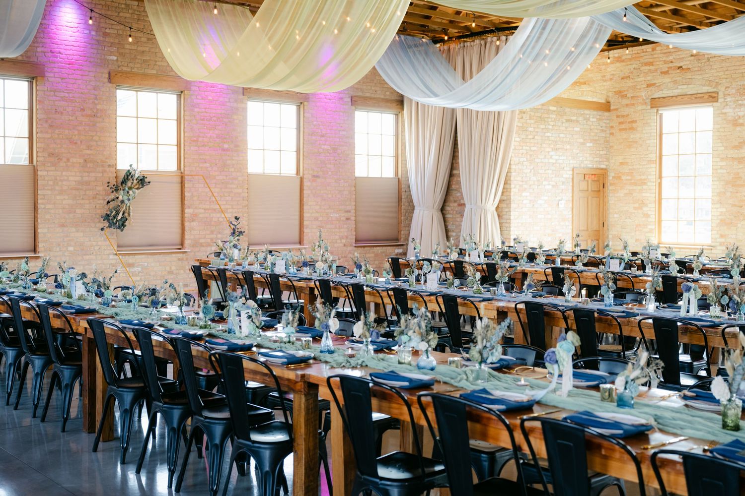 Elegant wedding reception hall with draped white fabric, purple lighting, and long tables set for a formal dinner. - The Brix on the Fox