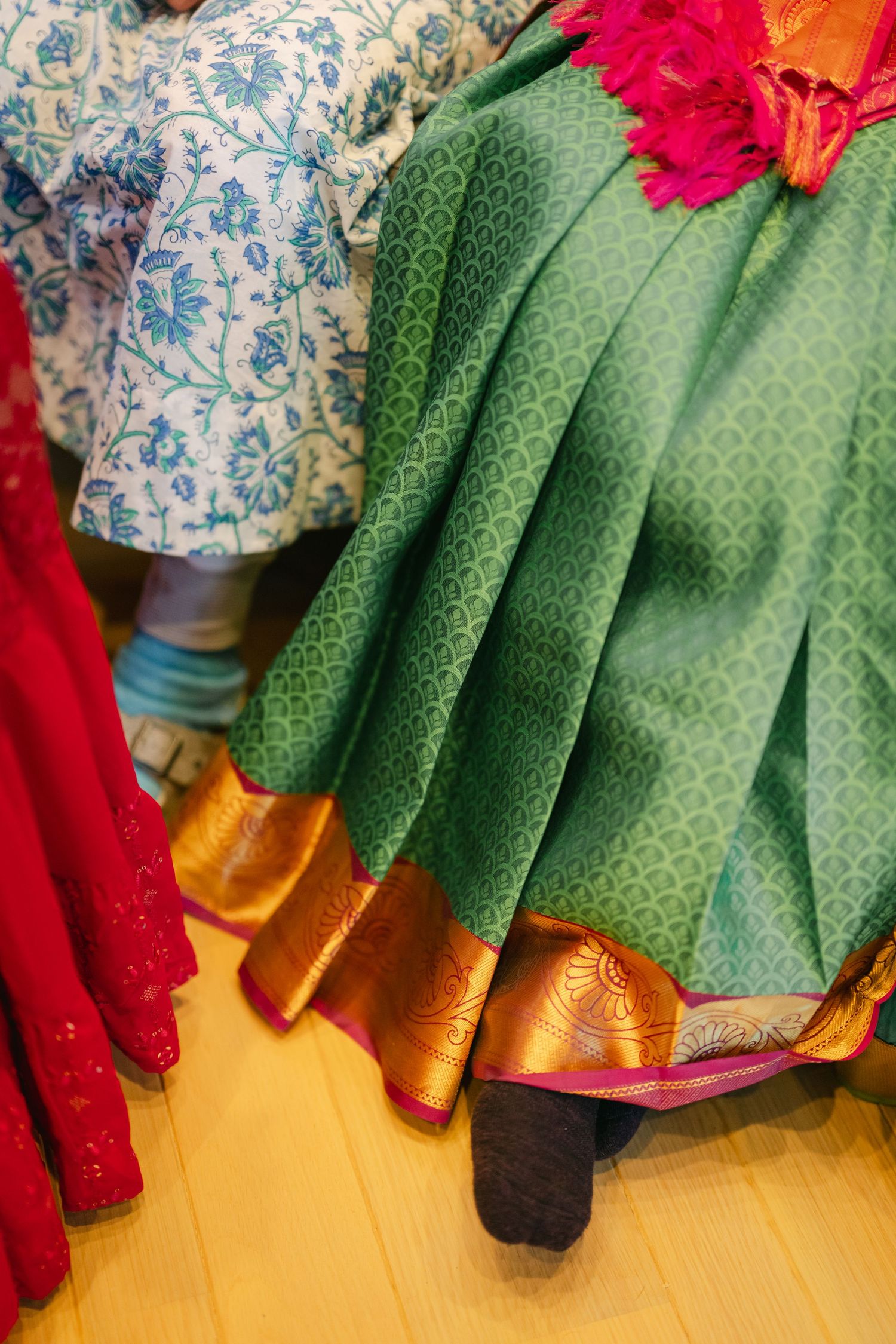 Traditional Indian clothing with green and gold silk sari with red accents displayed on wooden flooring.