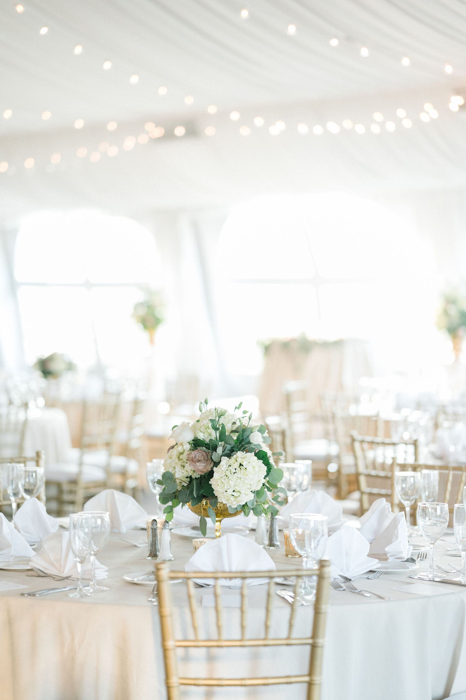 Dreamy white tent reception with elegant table settings and string lights overhead.