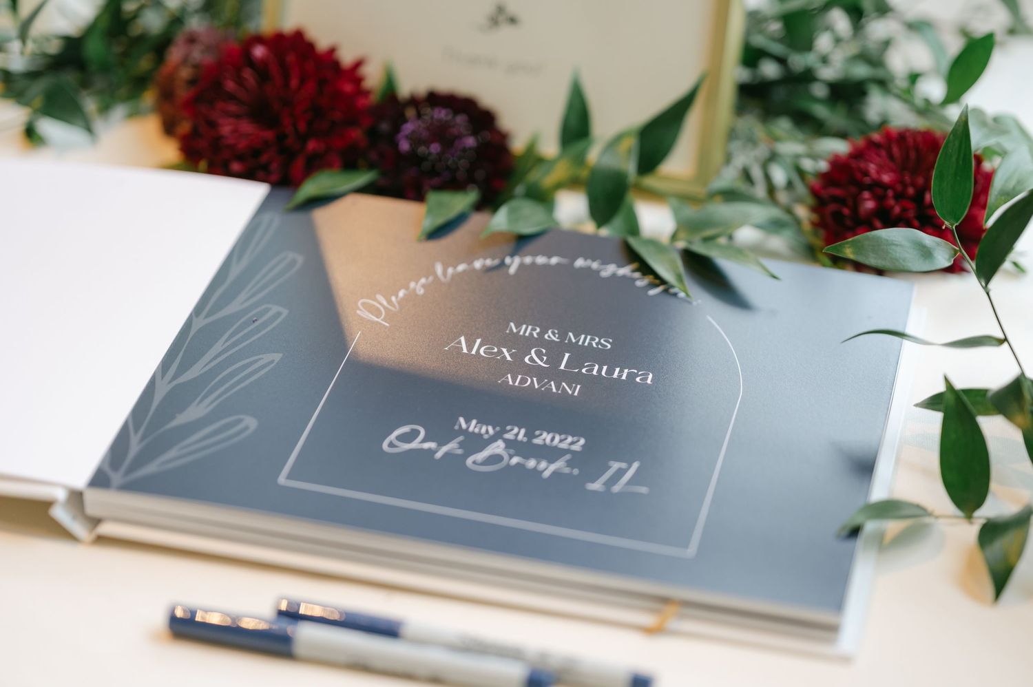 Gray wedding guest book with white calligraphy text surrounded by deep red roses and green foliage. - Hyatt Lodge Oak Brook