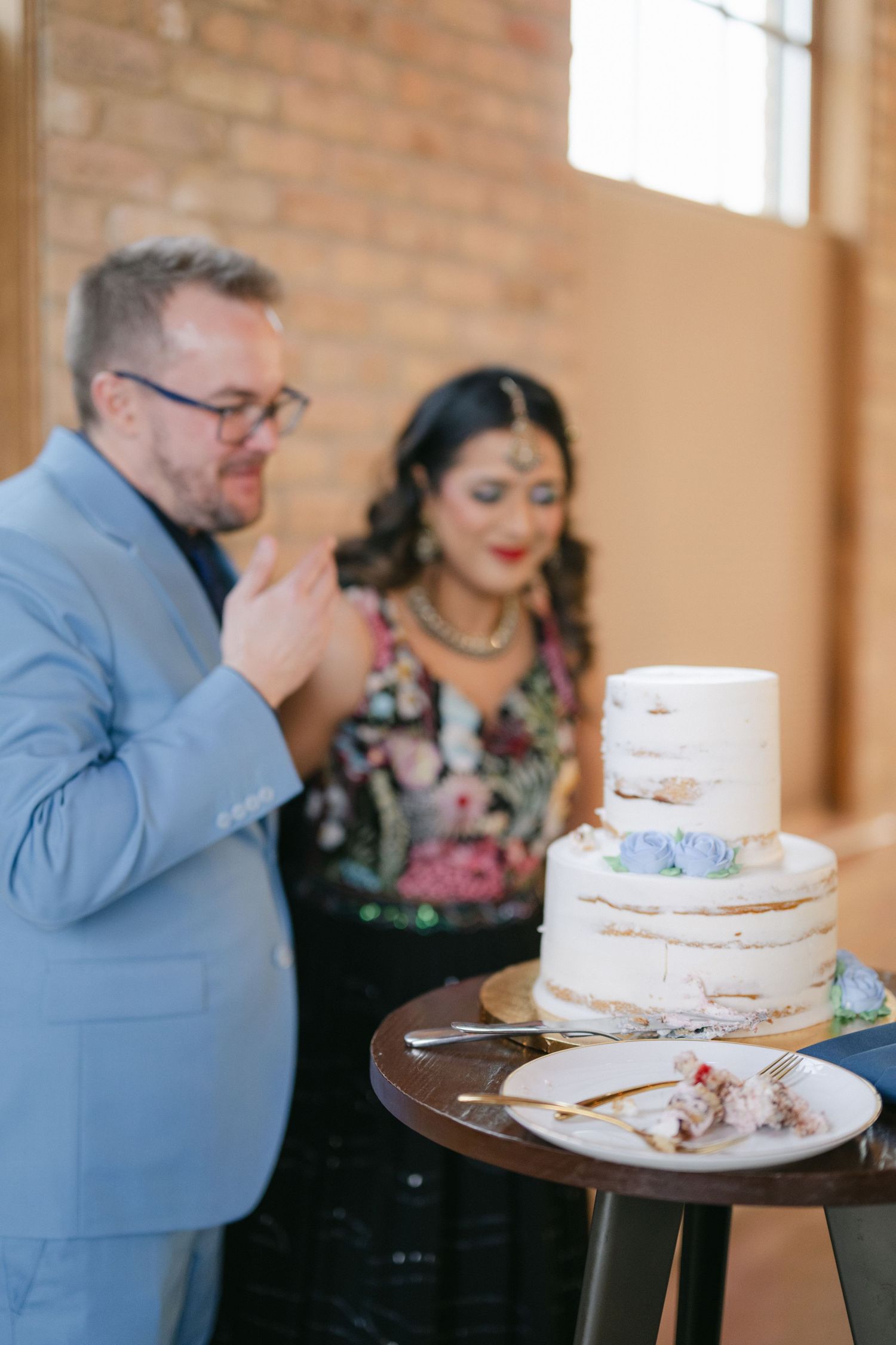 Two people share a slice of cake at a small round table in a rustic brick-walled room. - The Brix on the Fox
