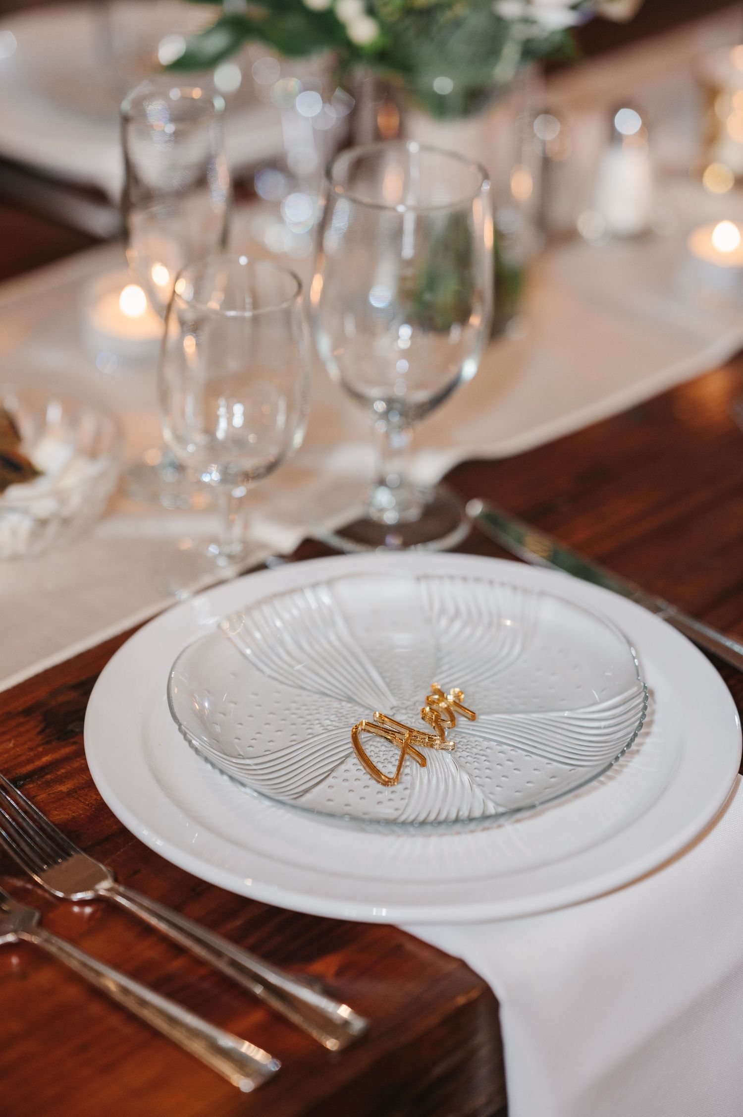 Elegant place setting with white plates and gold love sign decorations on a wooden table at a wedding reception.