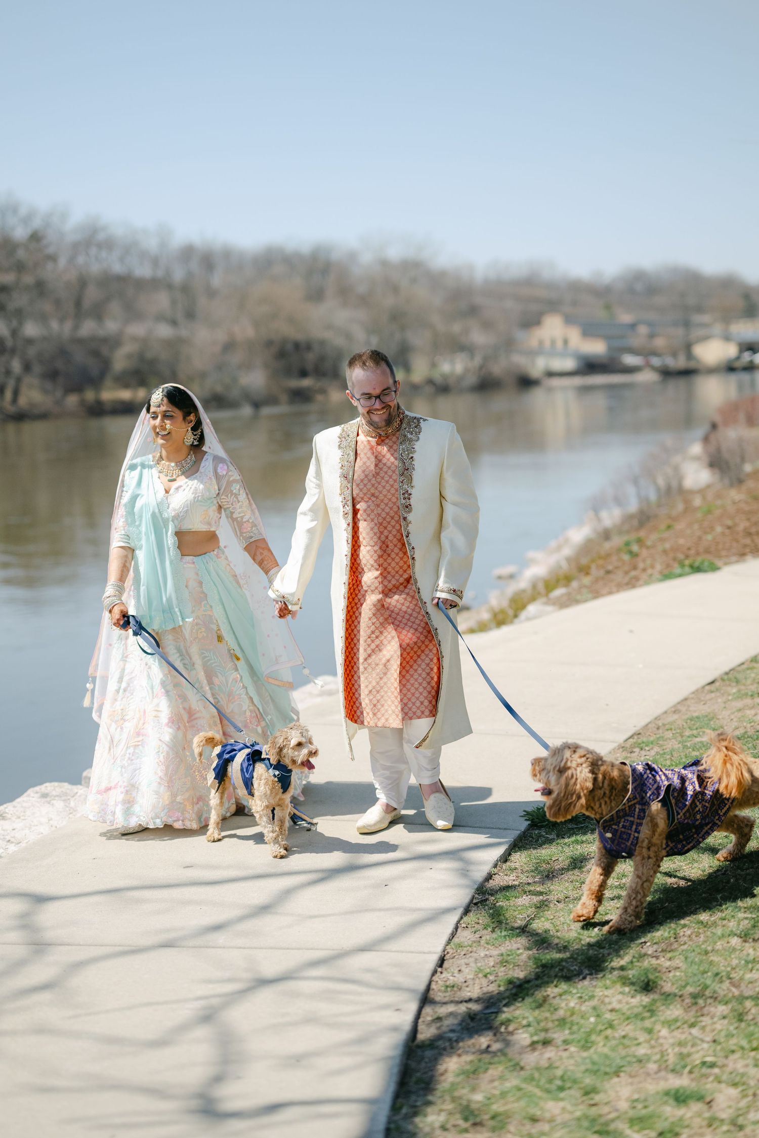 Two people in light colored dresses walk a small dog along a waterfront path on a sunny day. - The Brix on the Fox