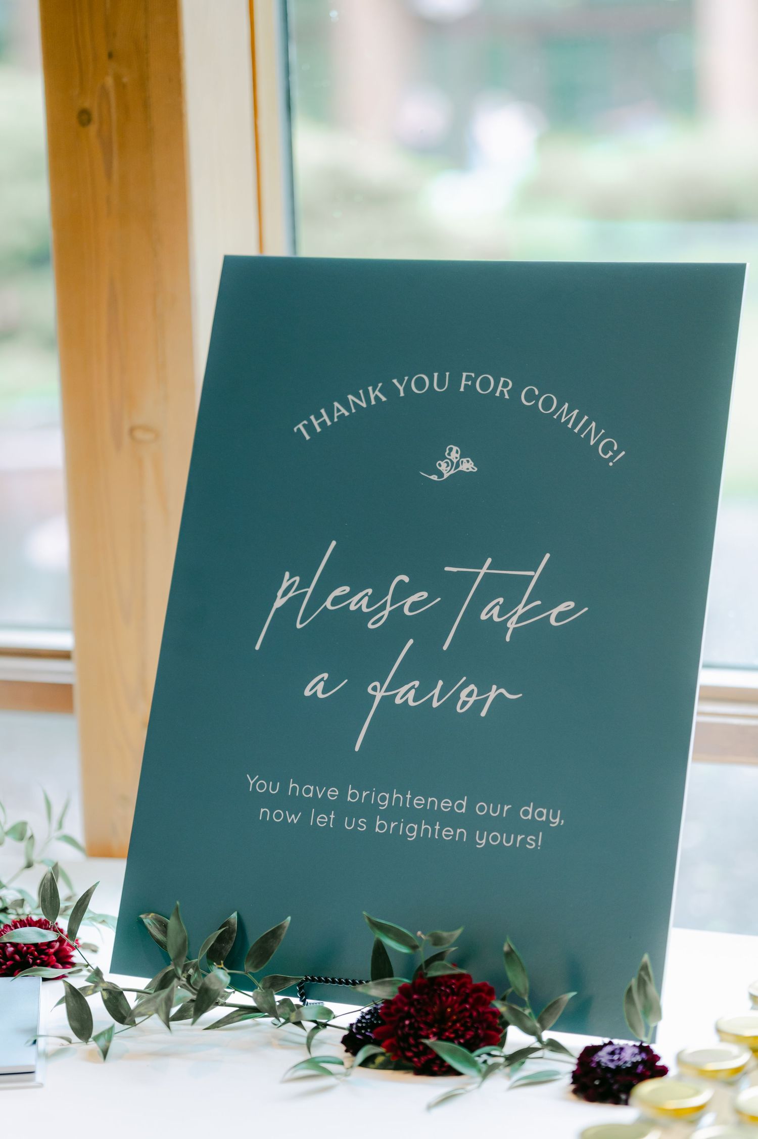 An elegant teal wedding sign reading 'Please take a favor' with decorative floral accents on a white table. - Hyatt Lodge Oak Brook
