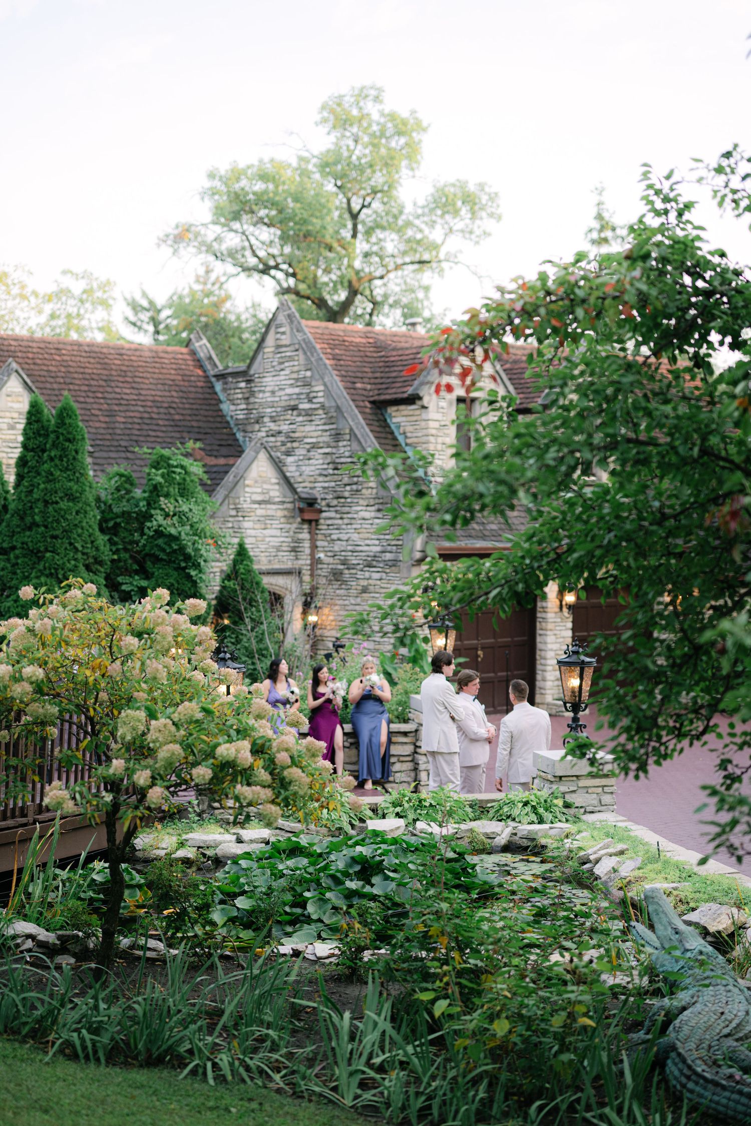 Stone cottage with lush garden pathway surrounded by blooming hydrangeas and greenery in an English countryside setting.